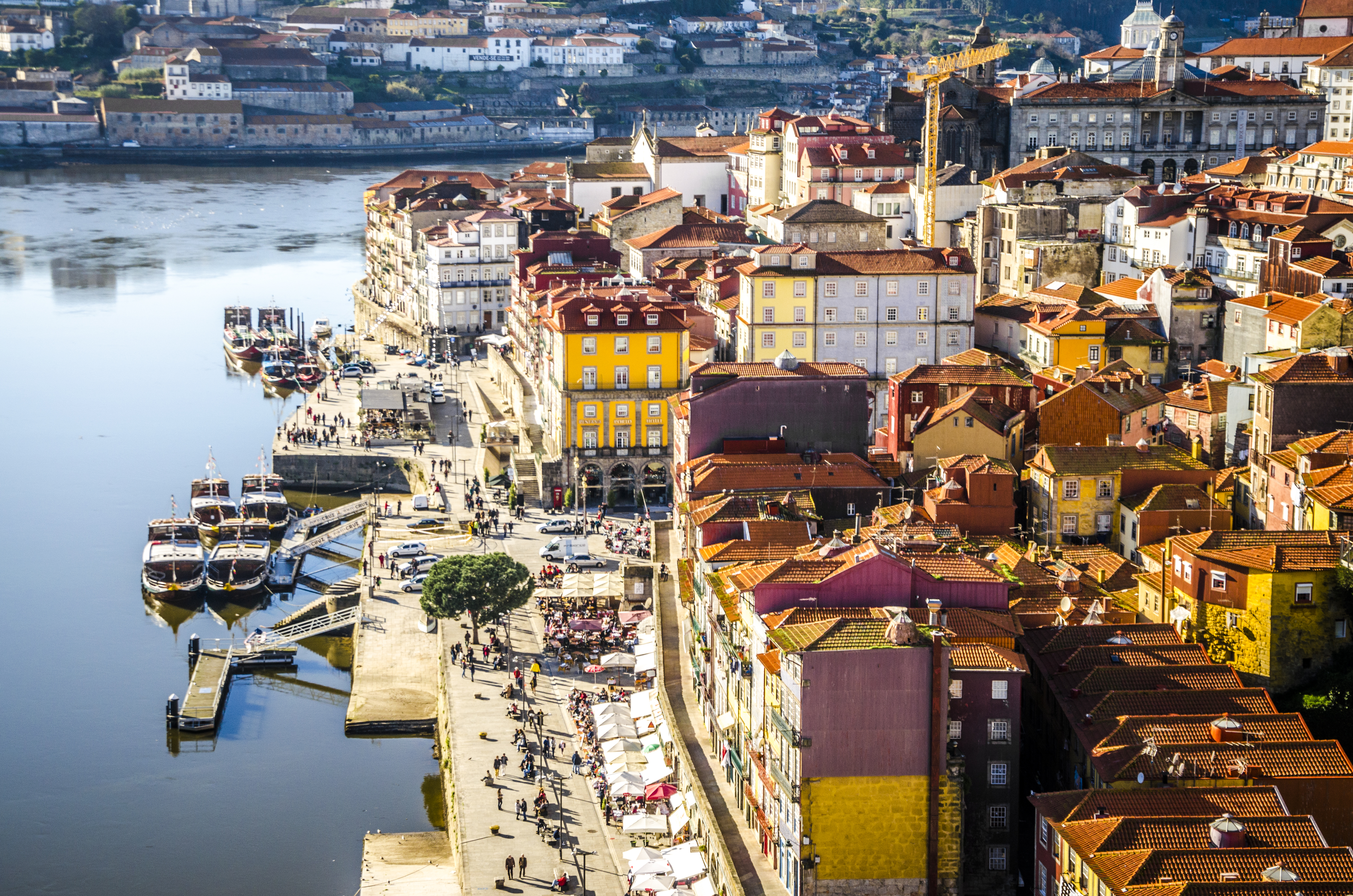 Aerial view of yellow buildings with brown tile roofs, with a bustling waterfront in Porto, Portugal