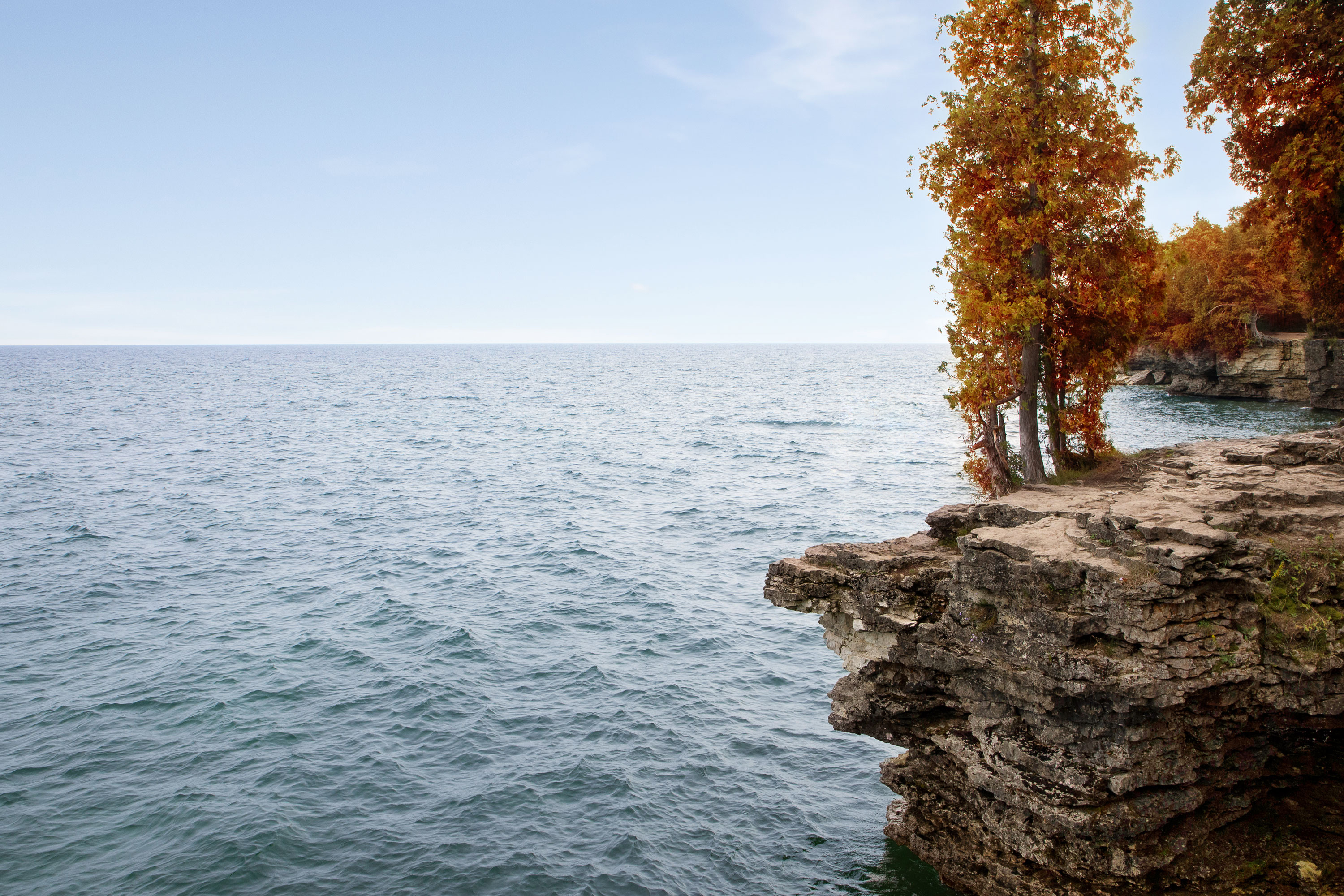 Flat, rocky cliff with orange trees stands at the edge of a vast lake in Door County, Wisconsin