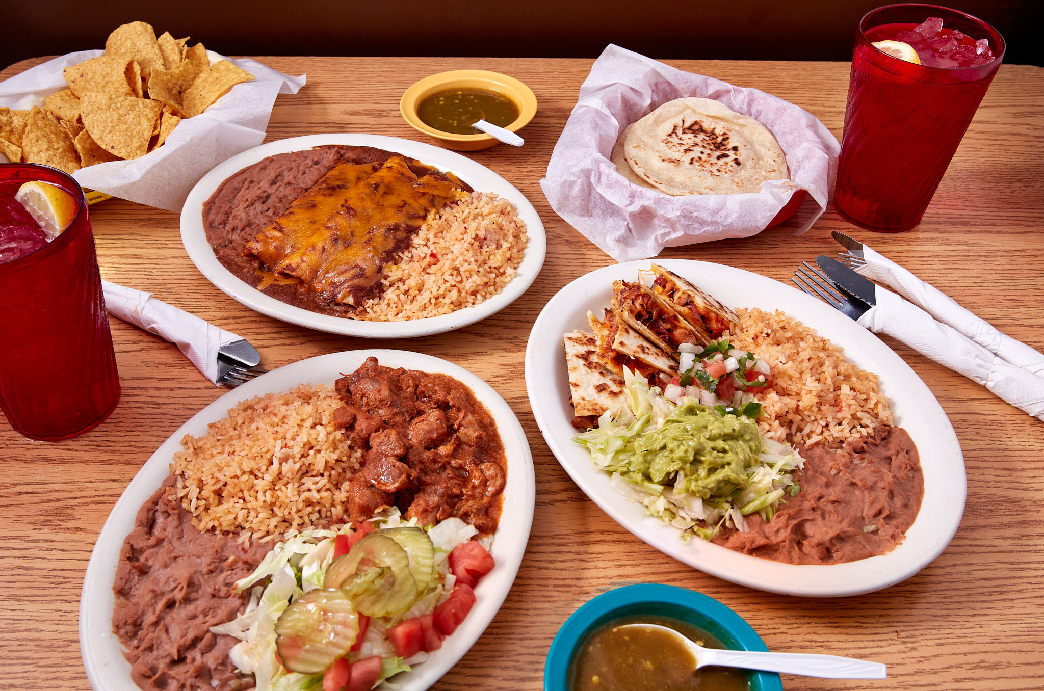 Wood table set with three plates of mexican food, sauces, and tortillas