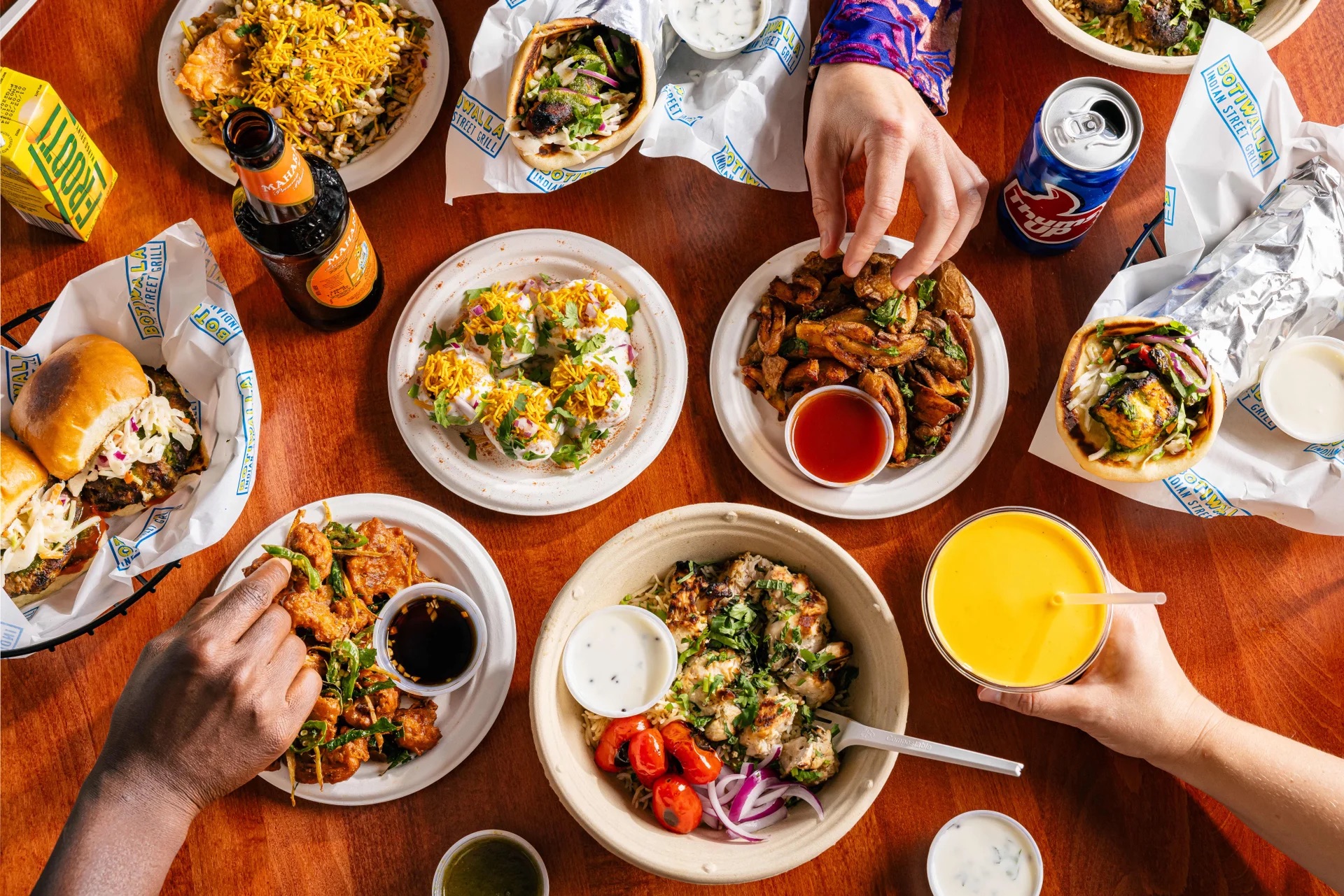 Five plates of Iranian-style dishes laid on a table, with hands grabbing at them