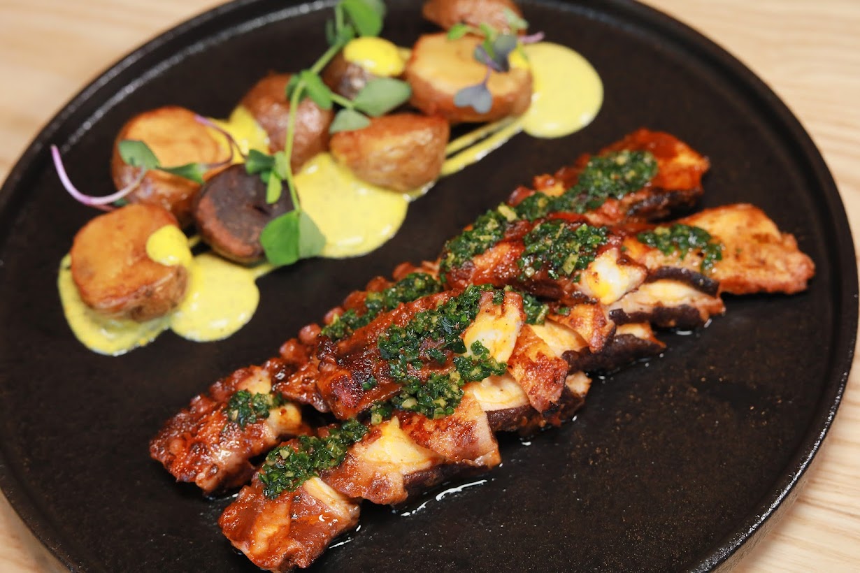 Octopus topped with green garnish and potatoes drizzled in yellow sauce