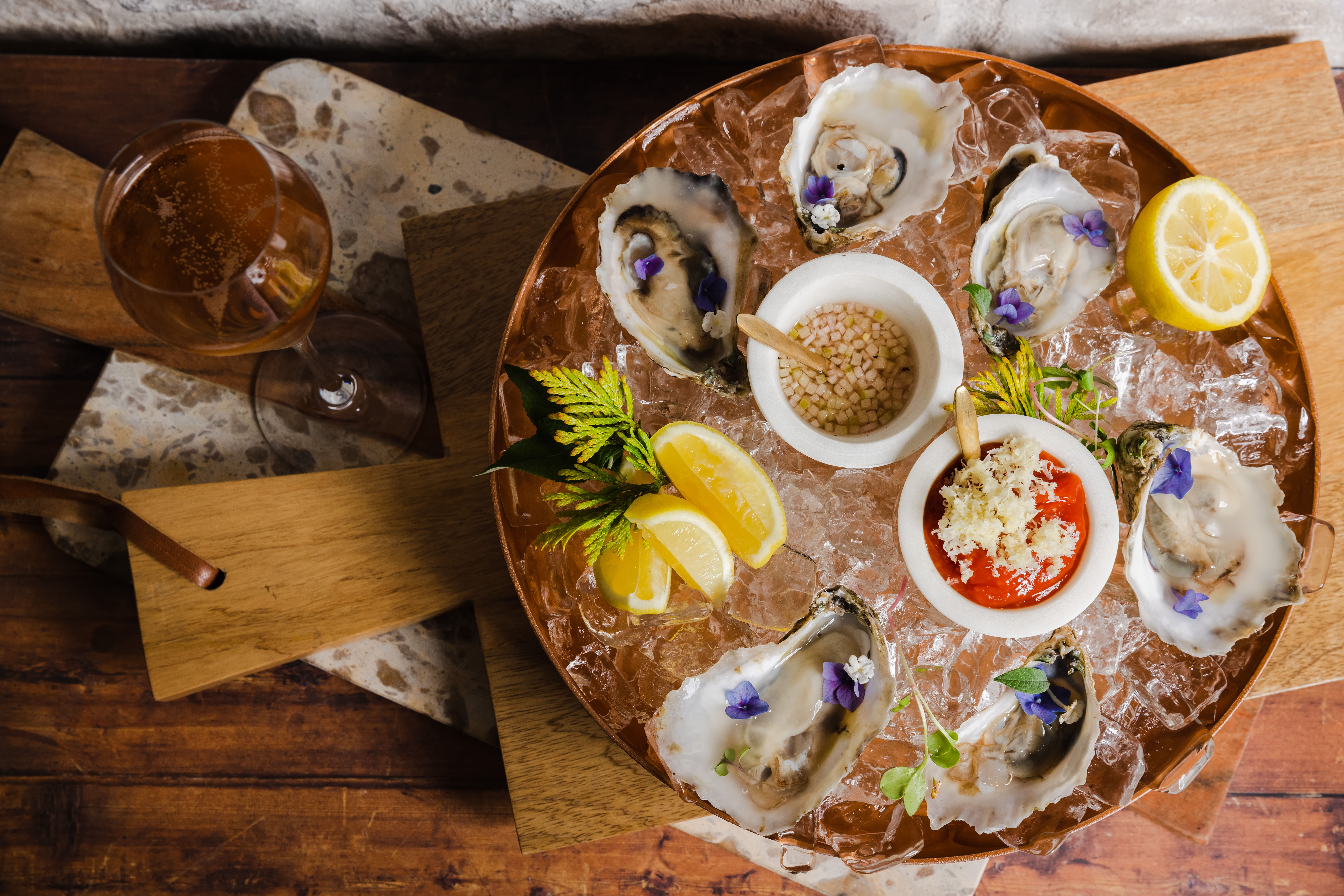 Oysters topped with blue edible flowers, served in a dish of ice with lemons and sauces