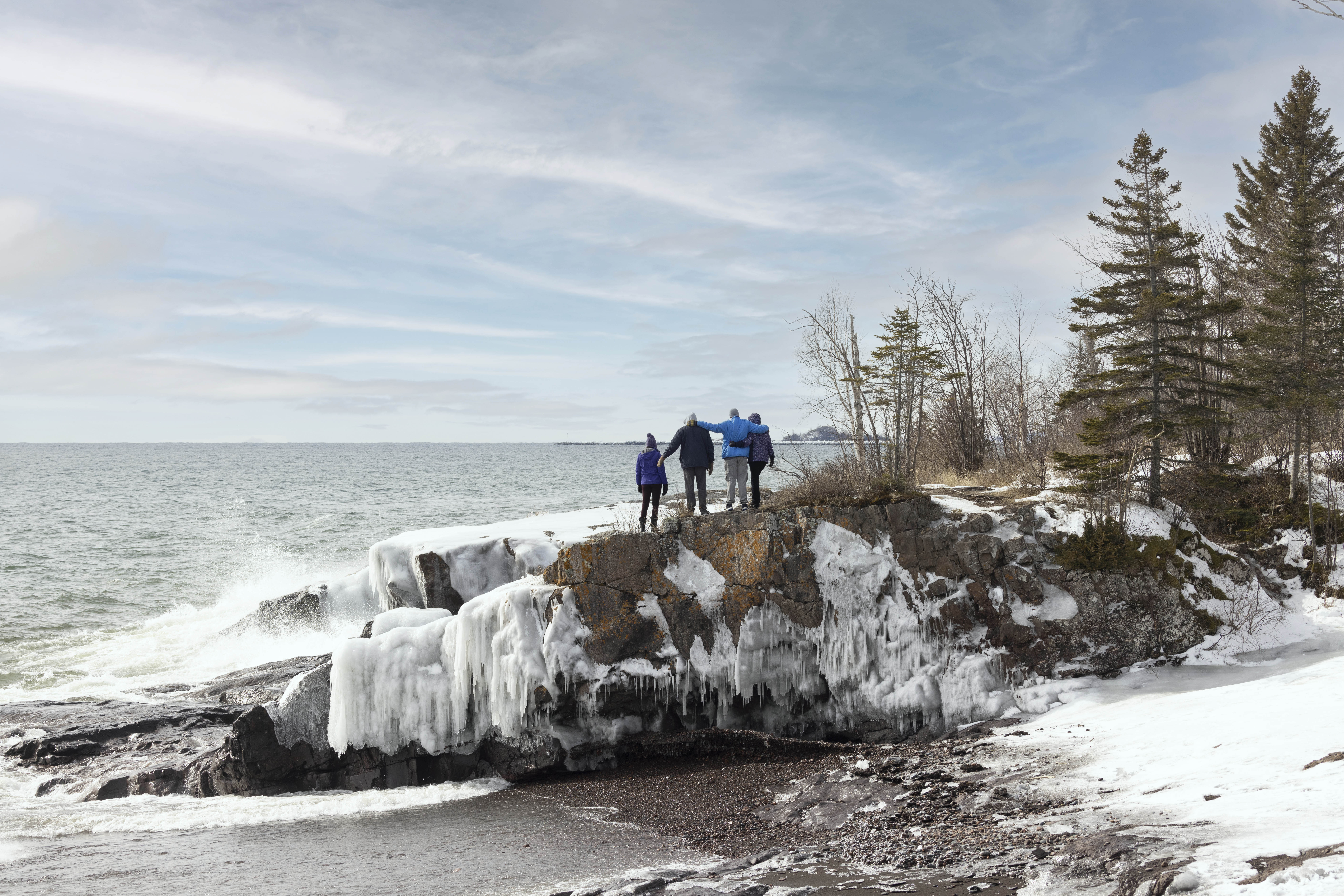 Four friends linking arms, standing on a rock formation on a snowy beach in winter