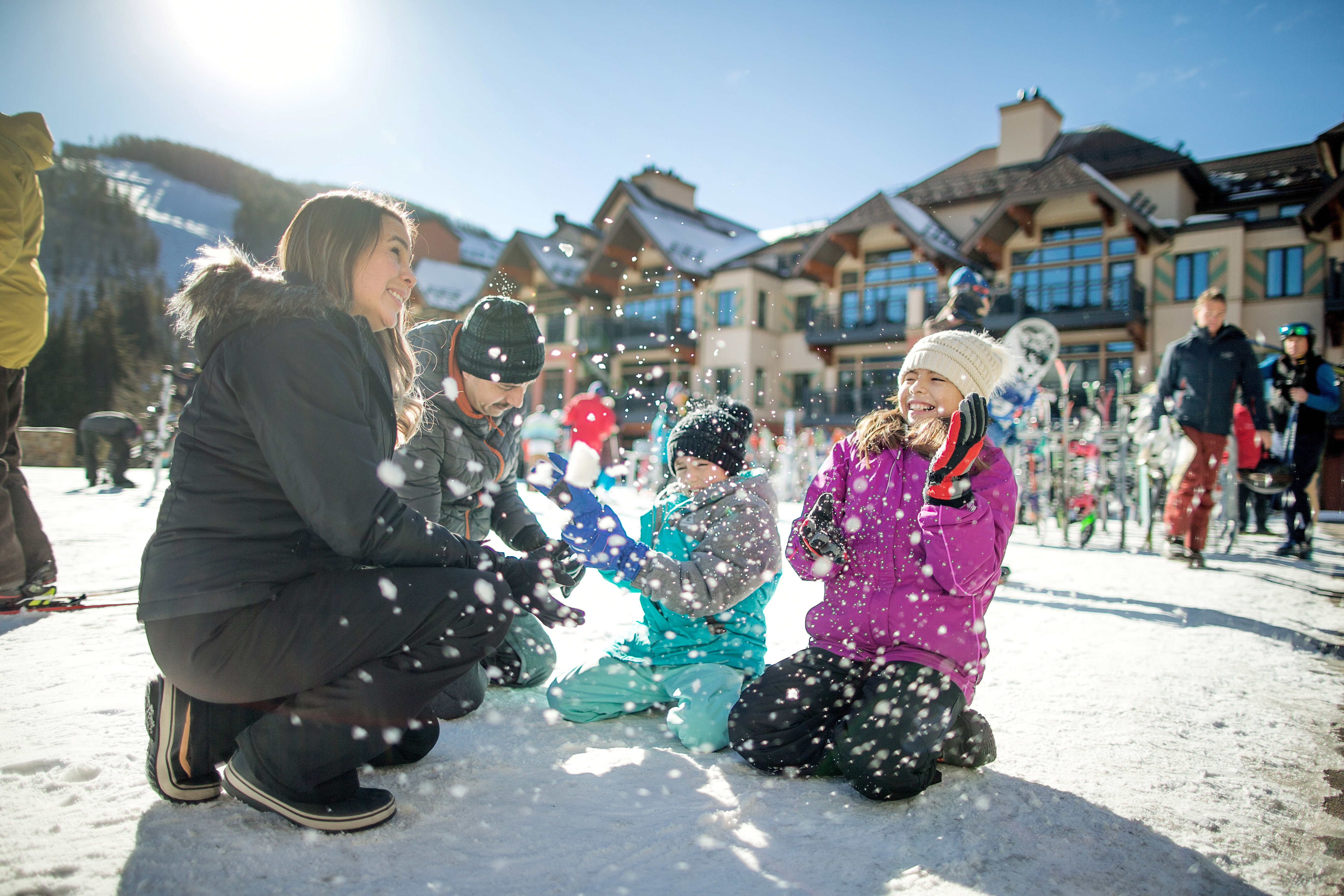 Family playing in the snow with a mountain lodge resort in the background