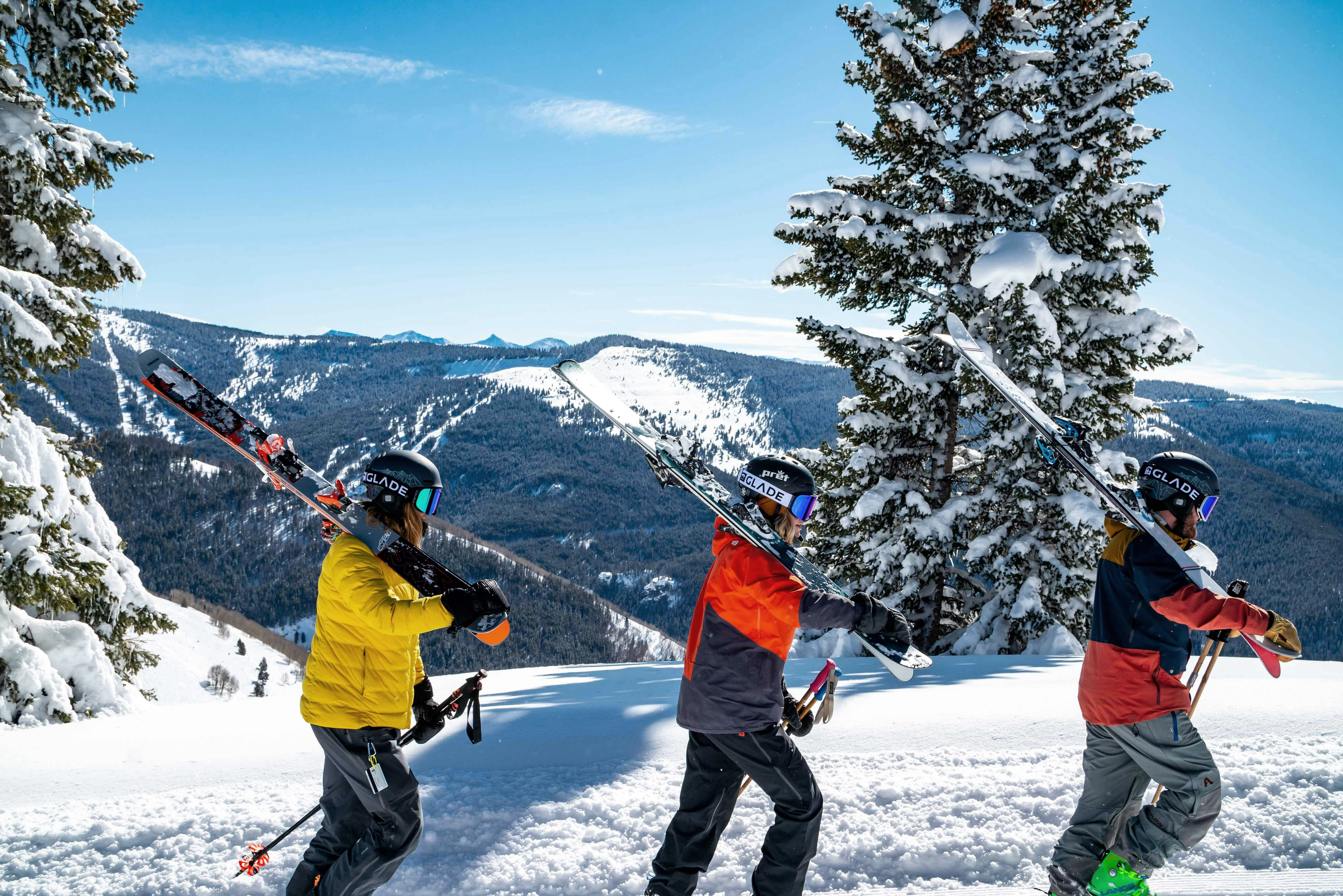 Three people walking in a row with their skis on their shoulders on a snowy mountain