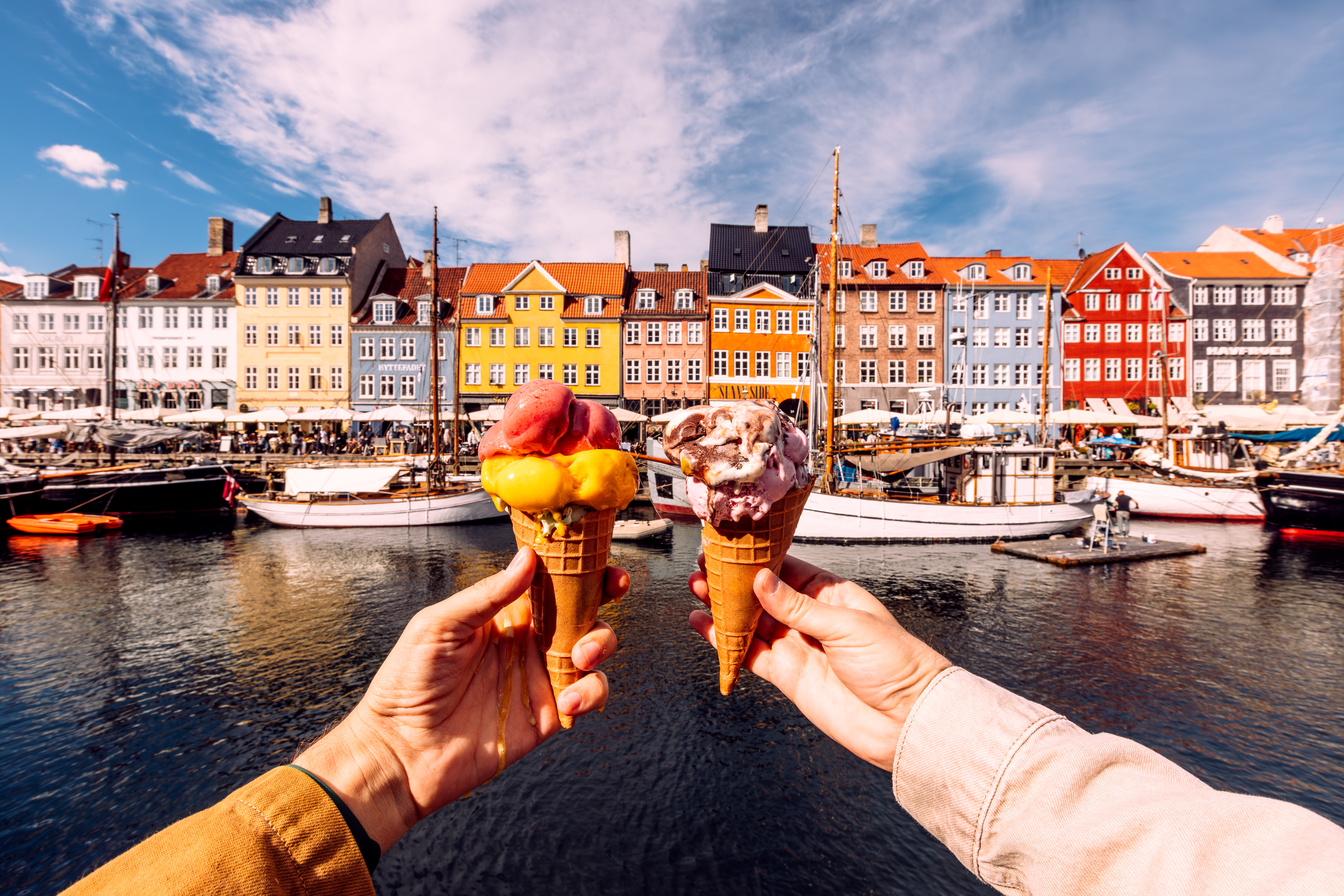 Two hands holding up colorful ice cream cones in front of the colorful row houses in Copenhagen
