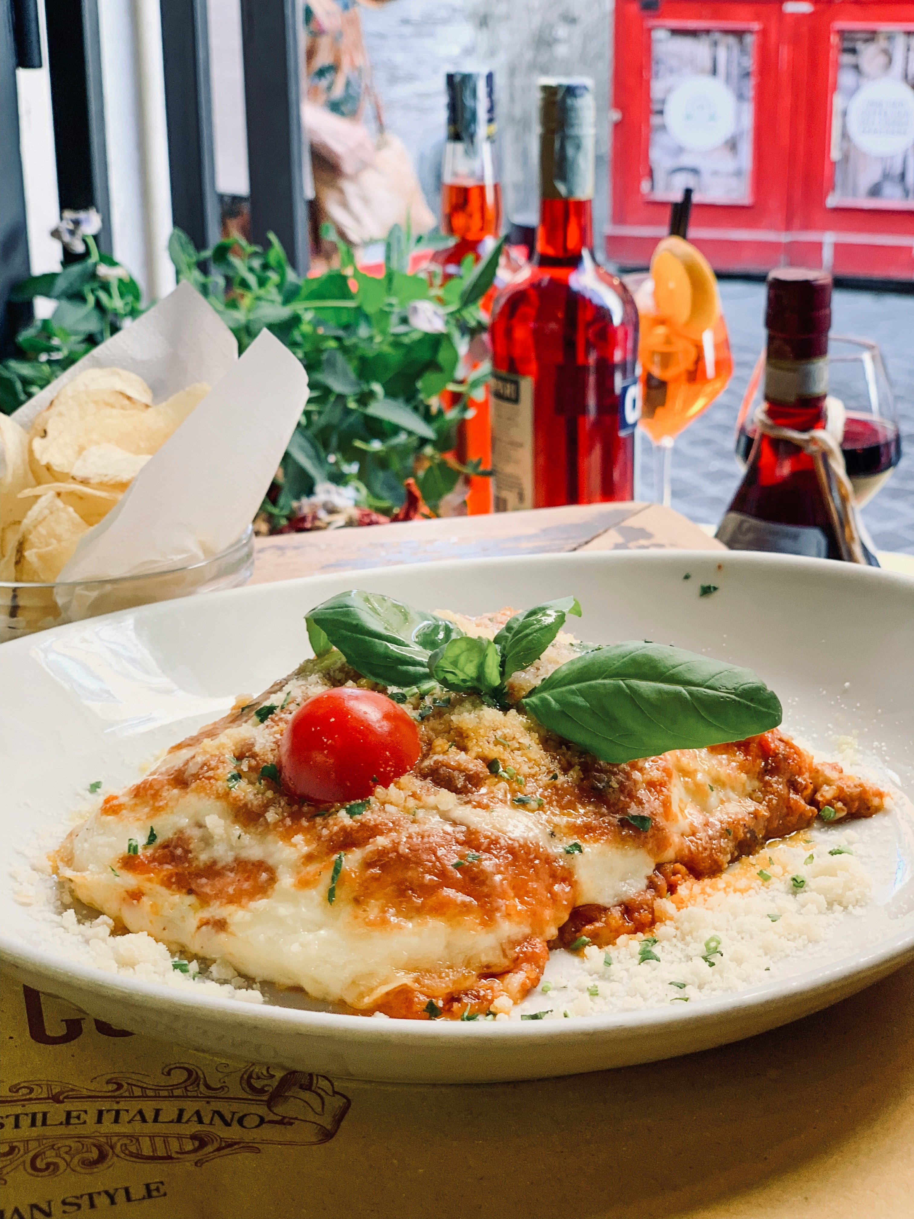 Dish of lasagna garnished with basil and a tomato with a view of the Roman street behind it