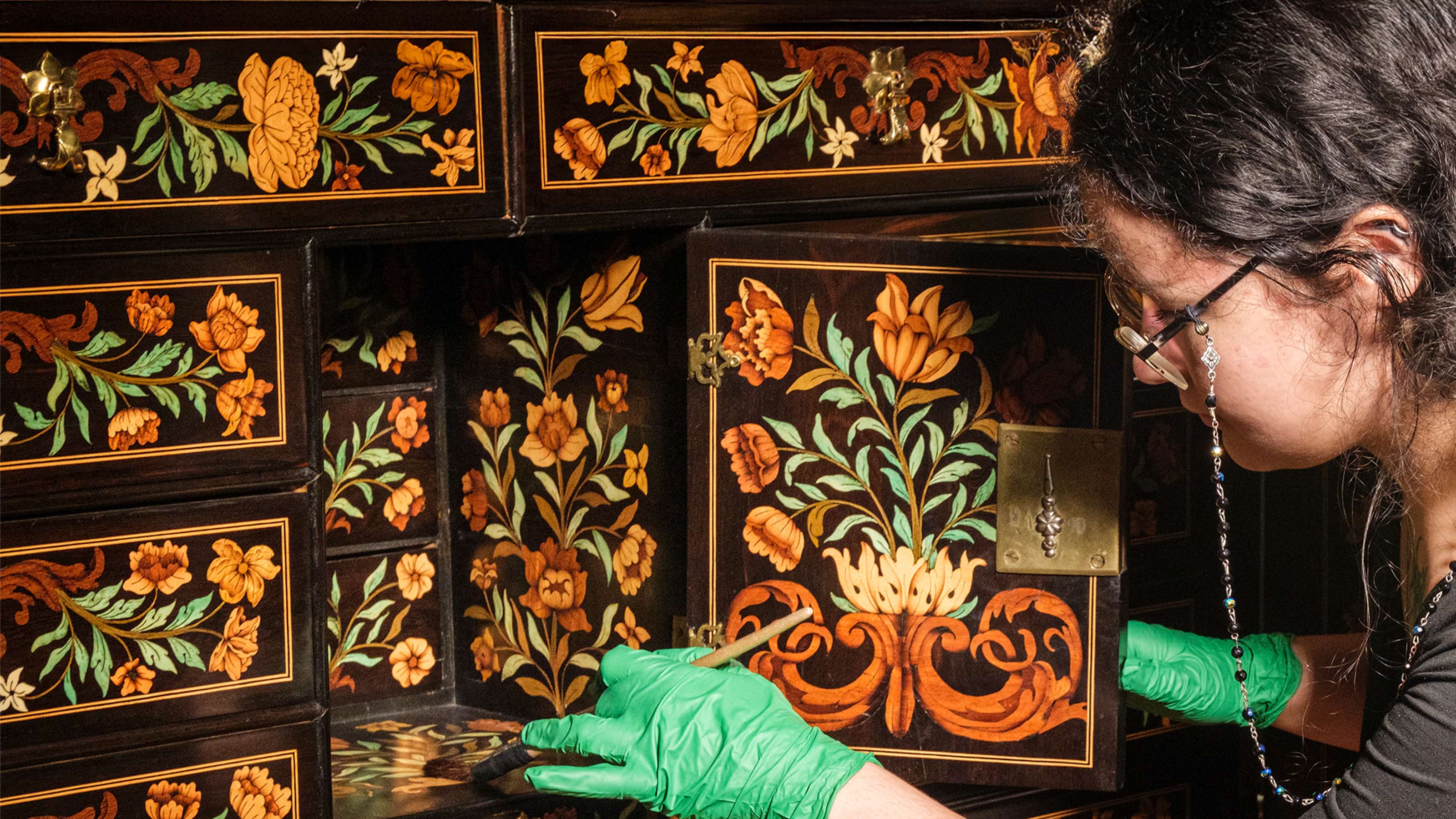 Person checking the condition of and cleaning an ornate colourfully decorated cabinet