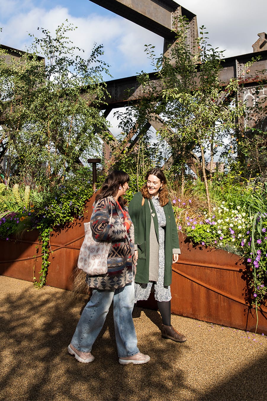 2 people walking along the Castlefield Viaduct sky park with raised  flower beds either side of the pathway 