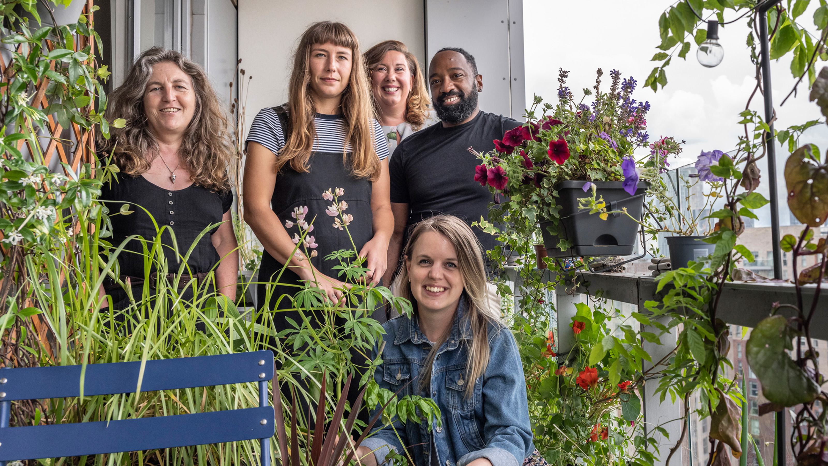 A group of five people stand on their apartment balcony surrounded by plants