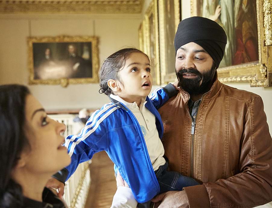 Parents with child in arms looking at portraits in a room at Ham House 