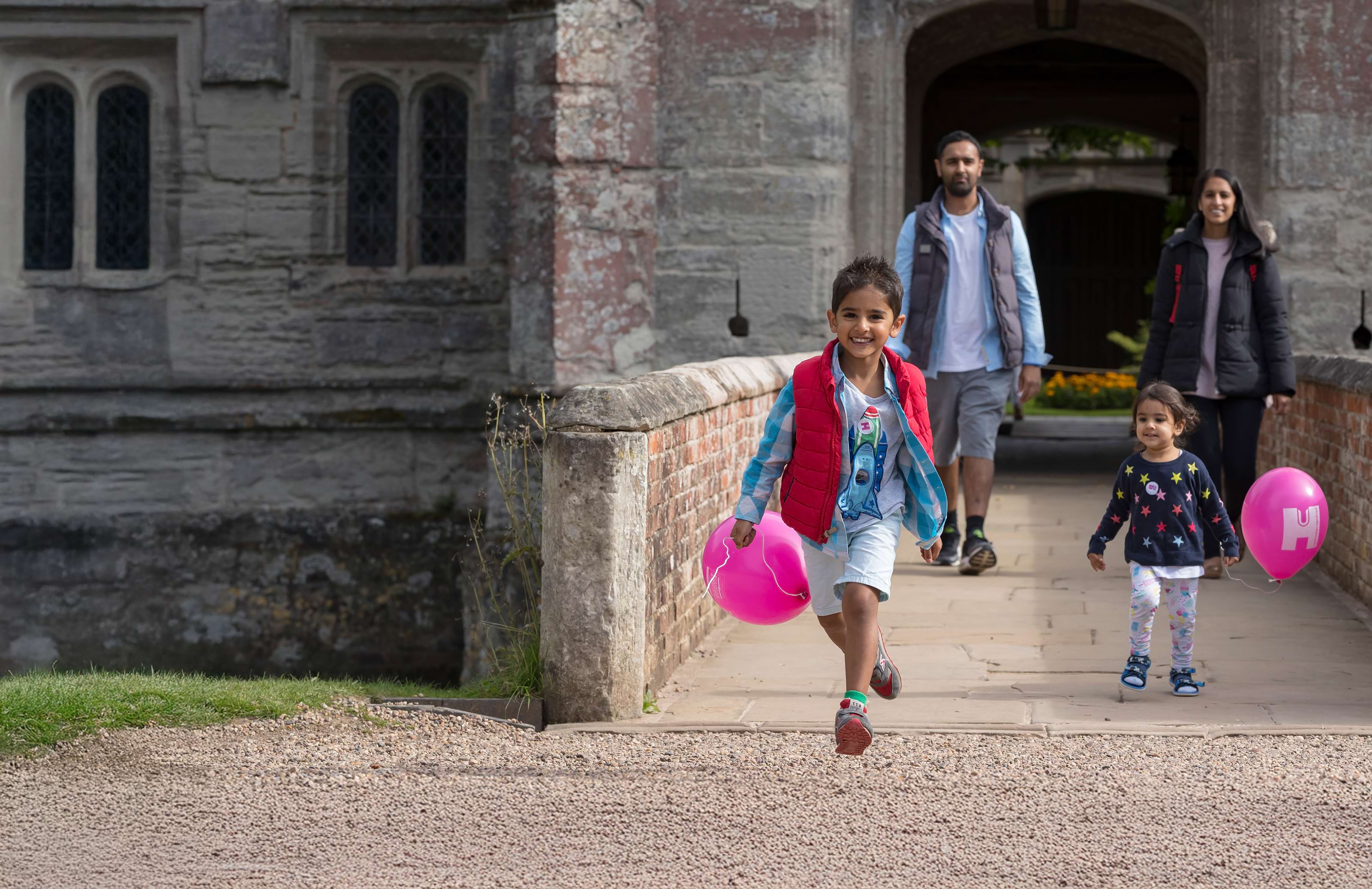Family of four exiting Baddesley Clinton. Children holding a pink balloon each and smiling