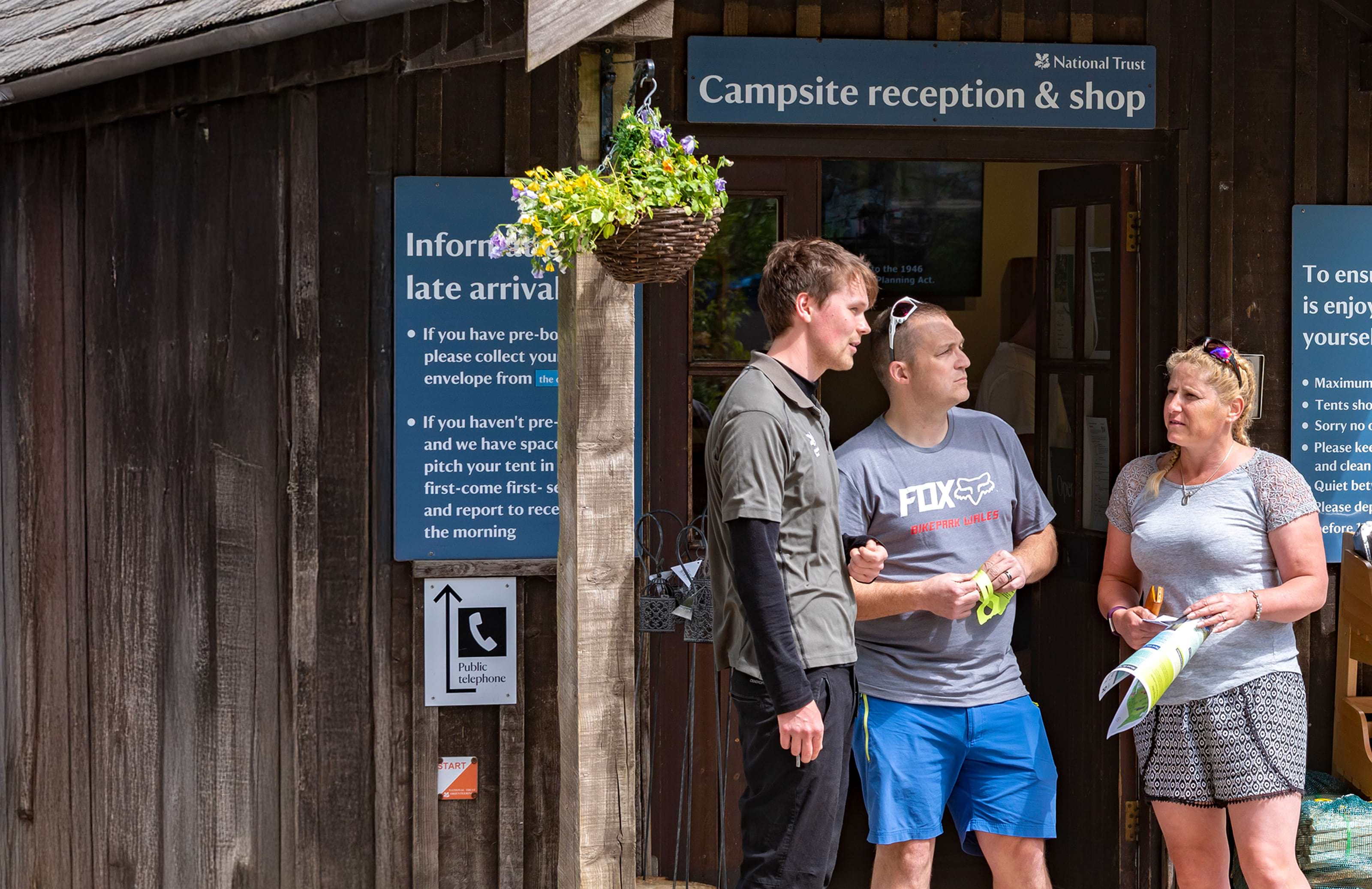 Staff member talking with visitors outside the reception area at Great Langdale campsite, Cumbria