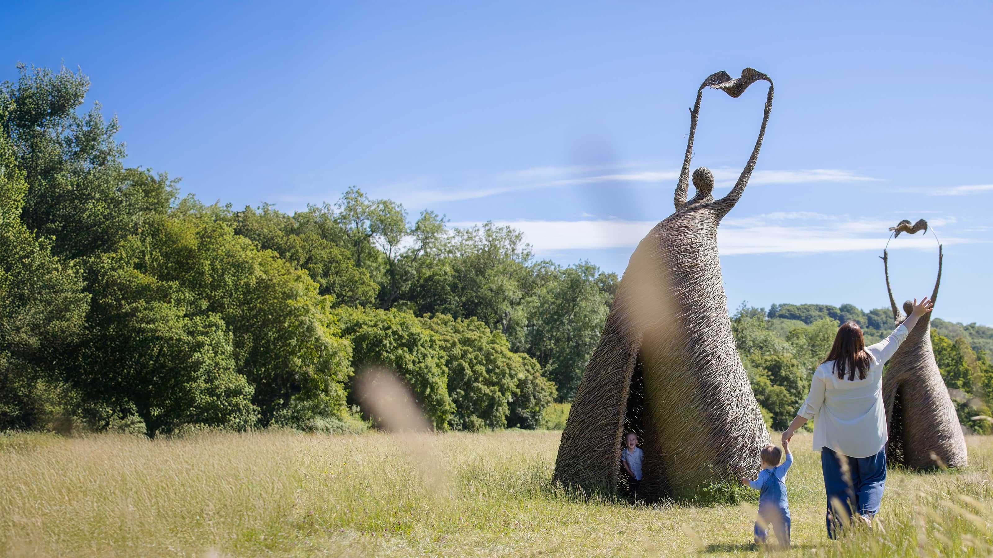 An adult and child looking at large willow sculptures in a meadow