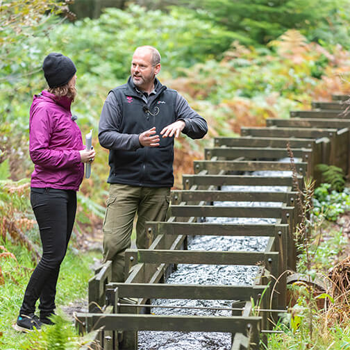 Two people stood by the hydro water course at Cragside, Northumberland 