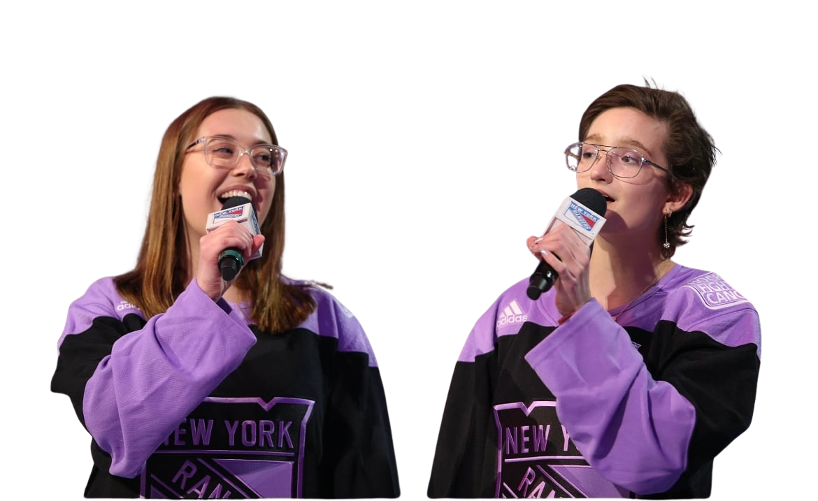 Person wearing a purple and black New York Rangers hockey jersey, speaking into a microphone. They are also wearing glasses.