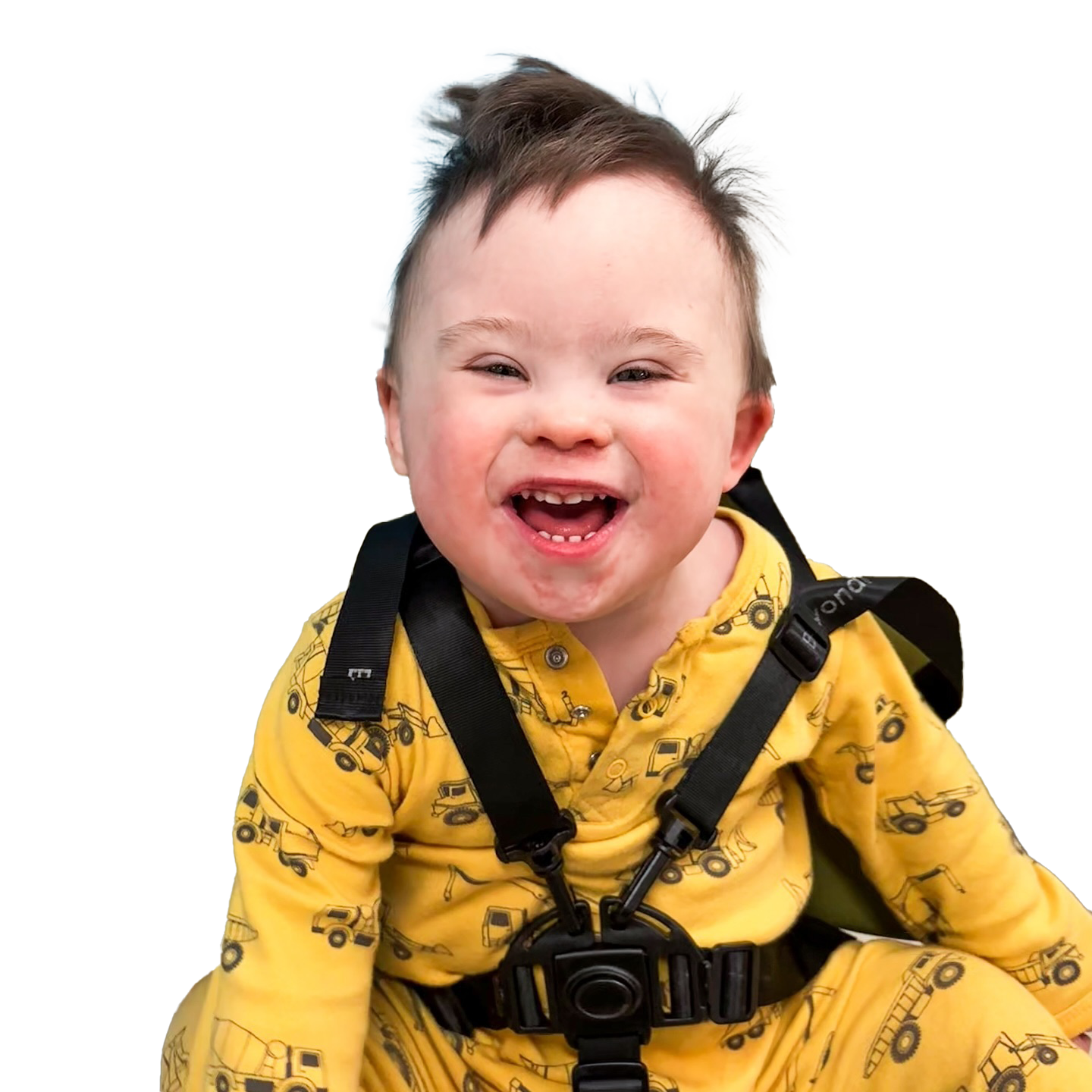 Young child wearing a yellow outfit with a construction vehicle pattern and black harness straps.