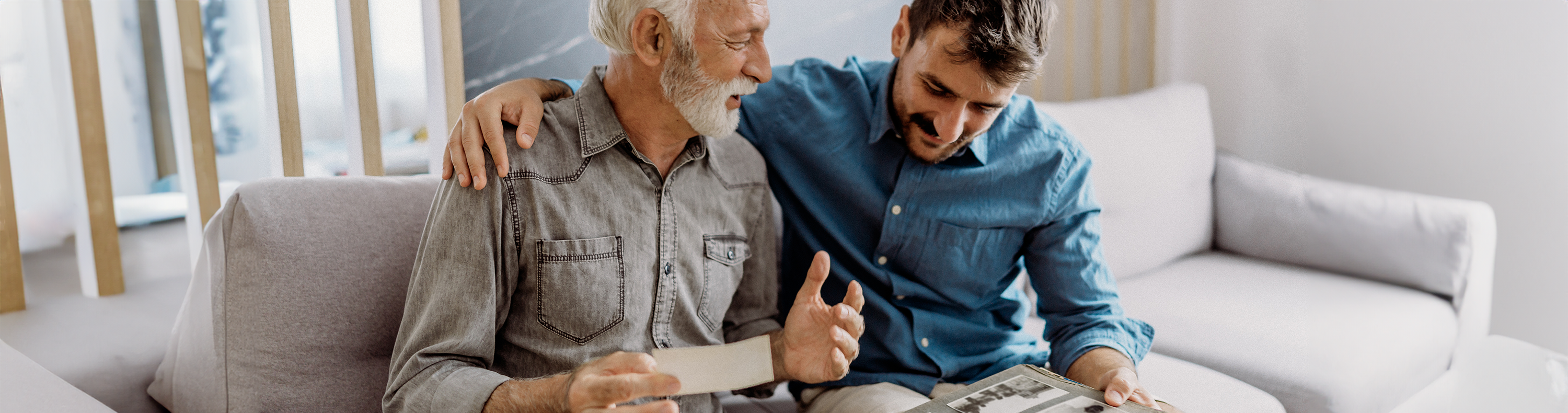 A man sitting on the couch with his father and looking through old photos