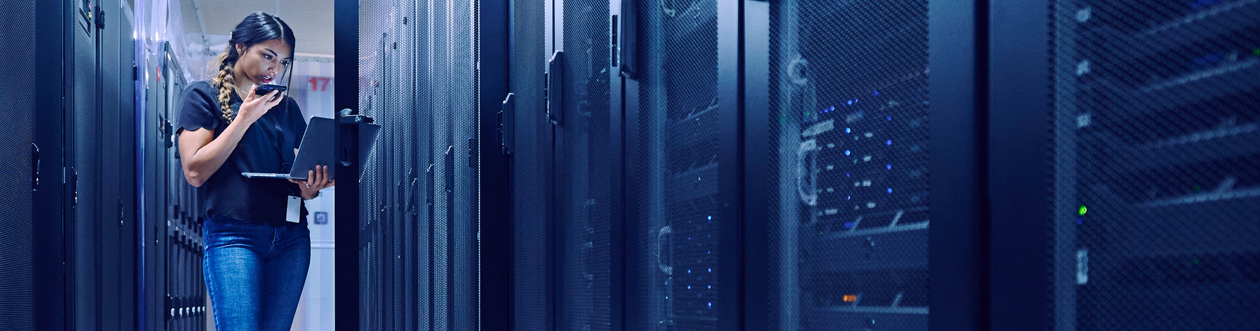 Female technician using laptop and phone in server room