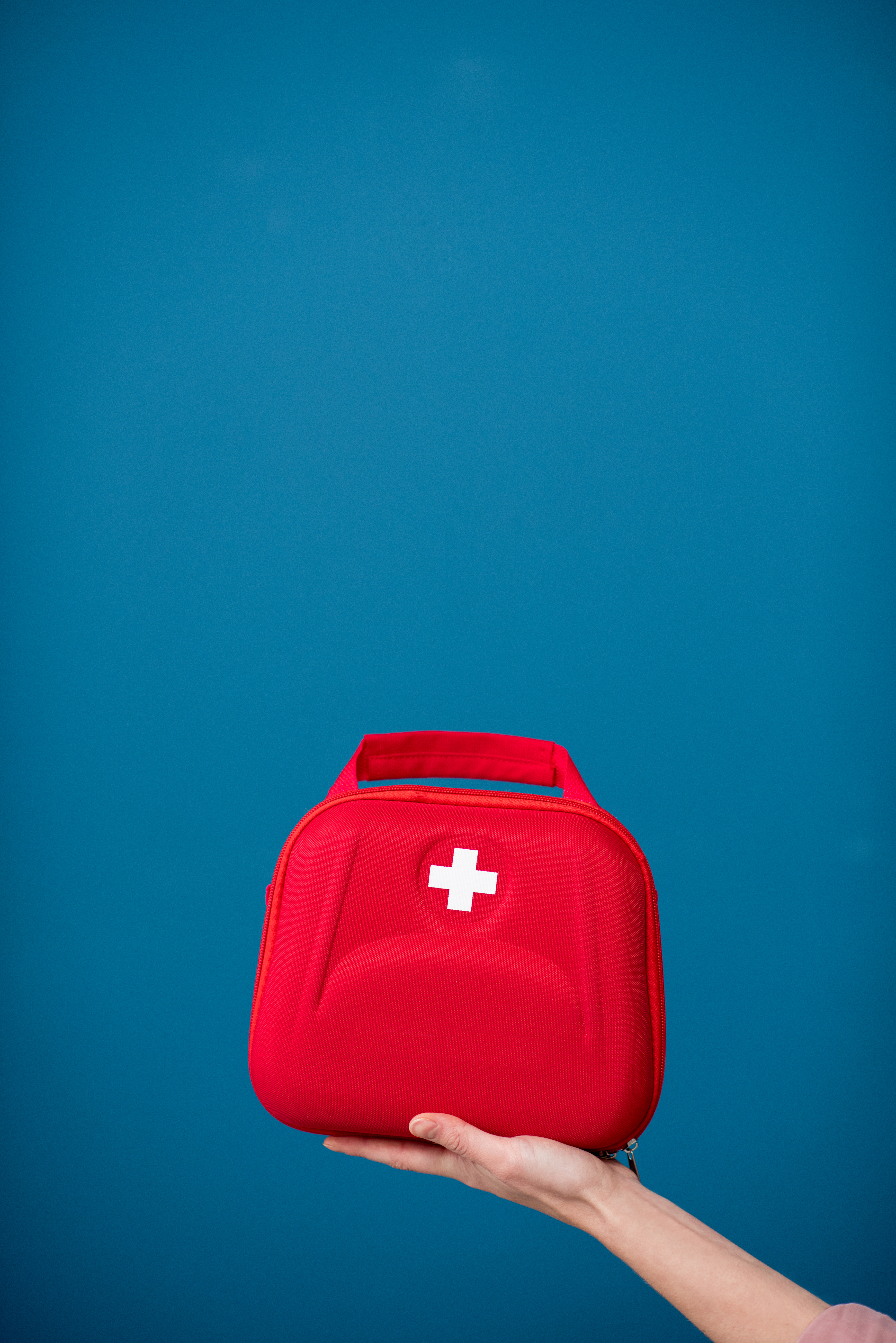 F - Follow safety guidelines. Image: A red medical kit with a white medical cross is being supported by a hand on a blue background. Understanding and following safety practices is important. 
