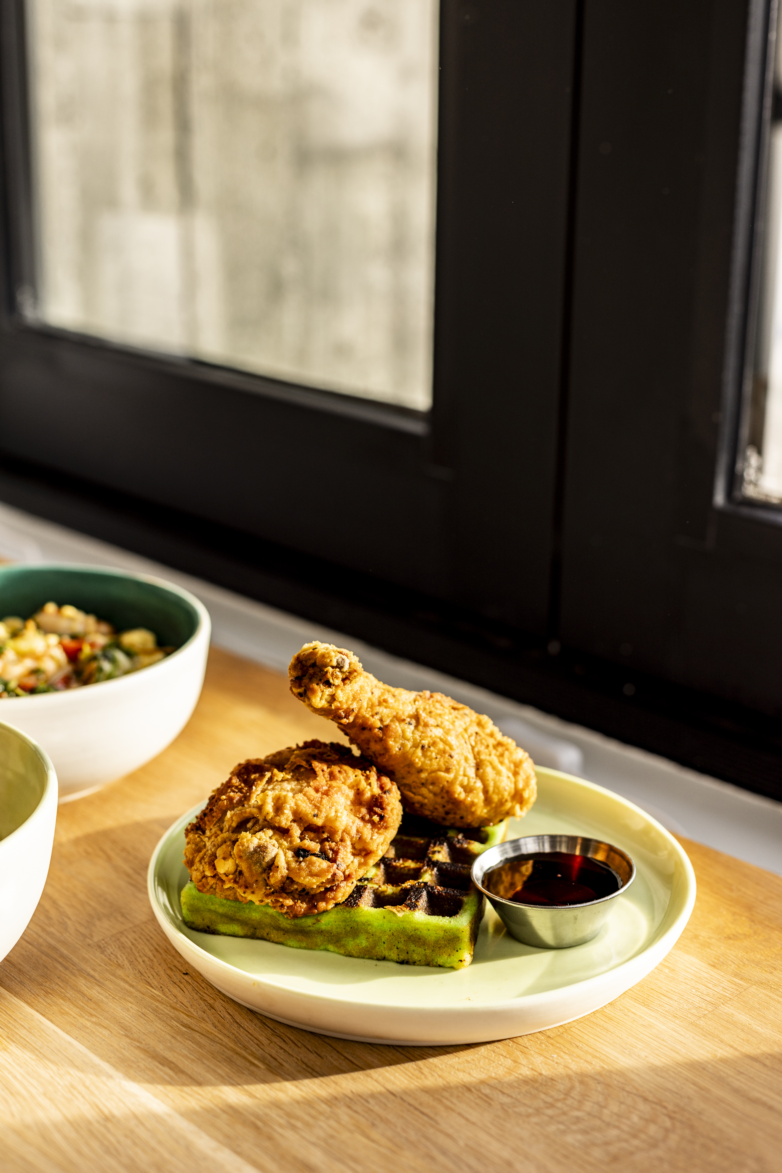 A pandan waffle topped with fried chicken with a dish of maple syrup
