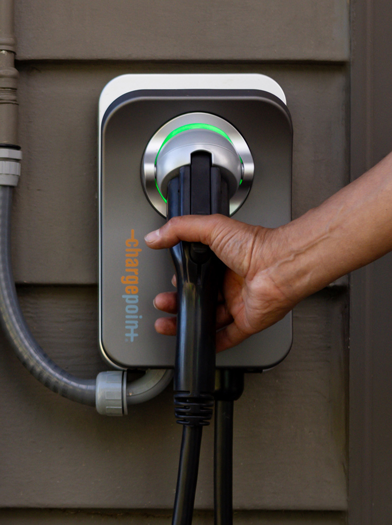 Hand holding the connector of a ChargePoint Level 2 charger mounted on the side of a building. 