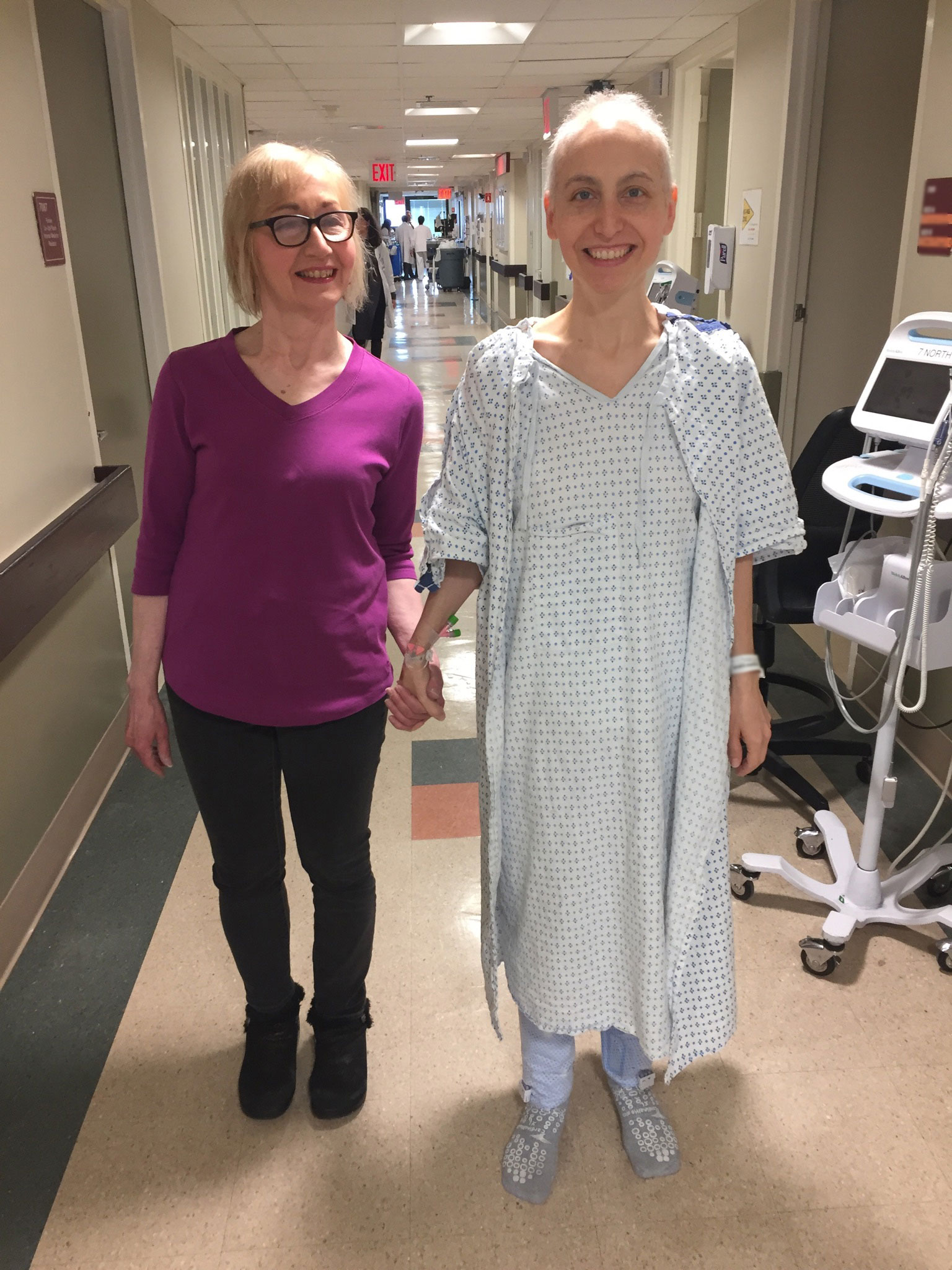 Females standing hand-in-hand hospital corridor.