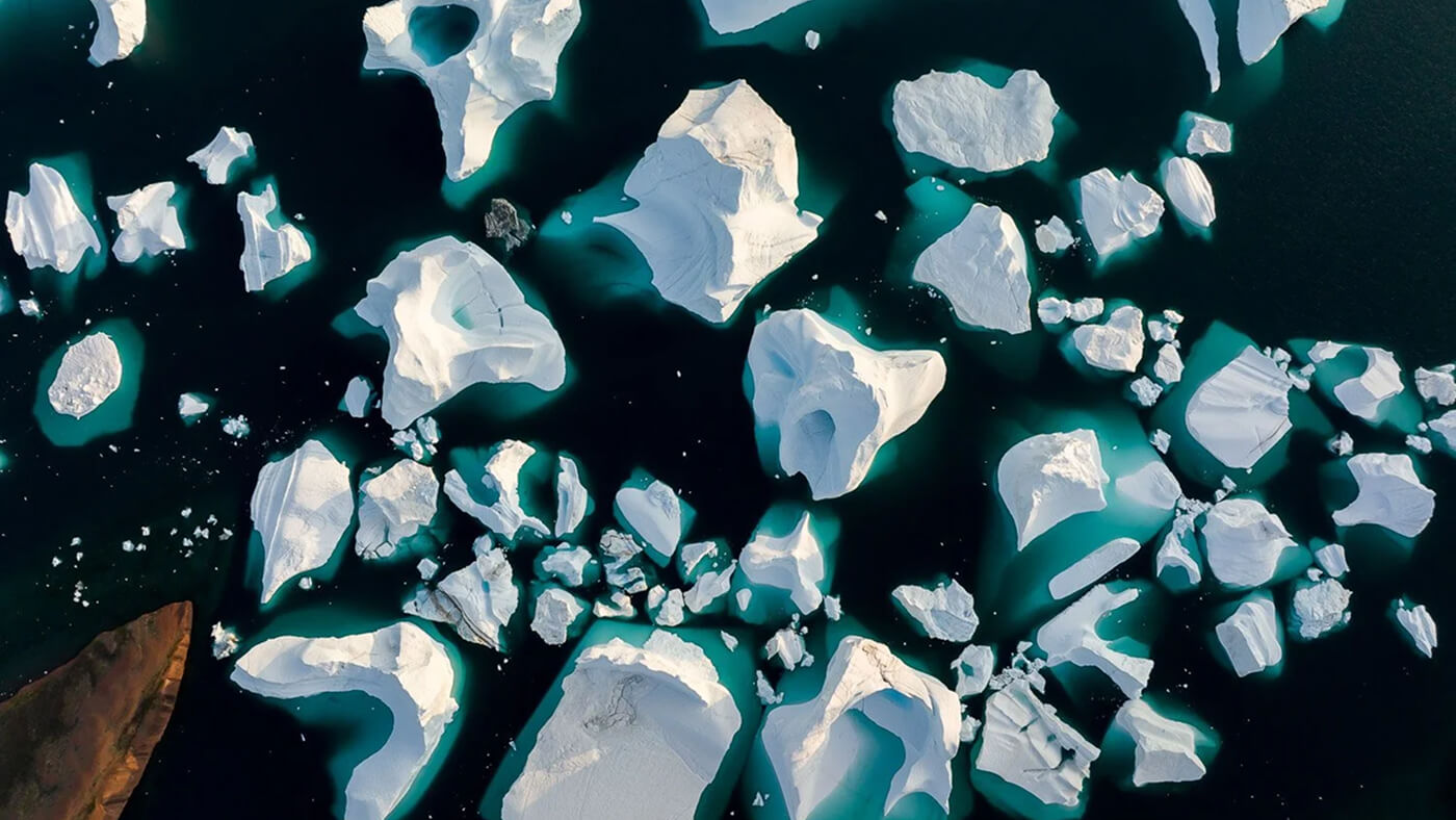 Aerial view of scattered icebergs floating in dark blue water with turquoise highlights.