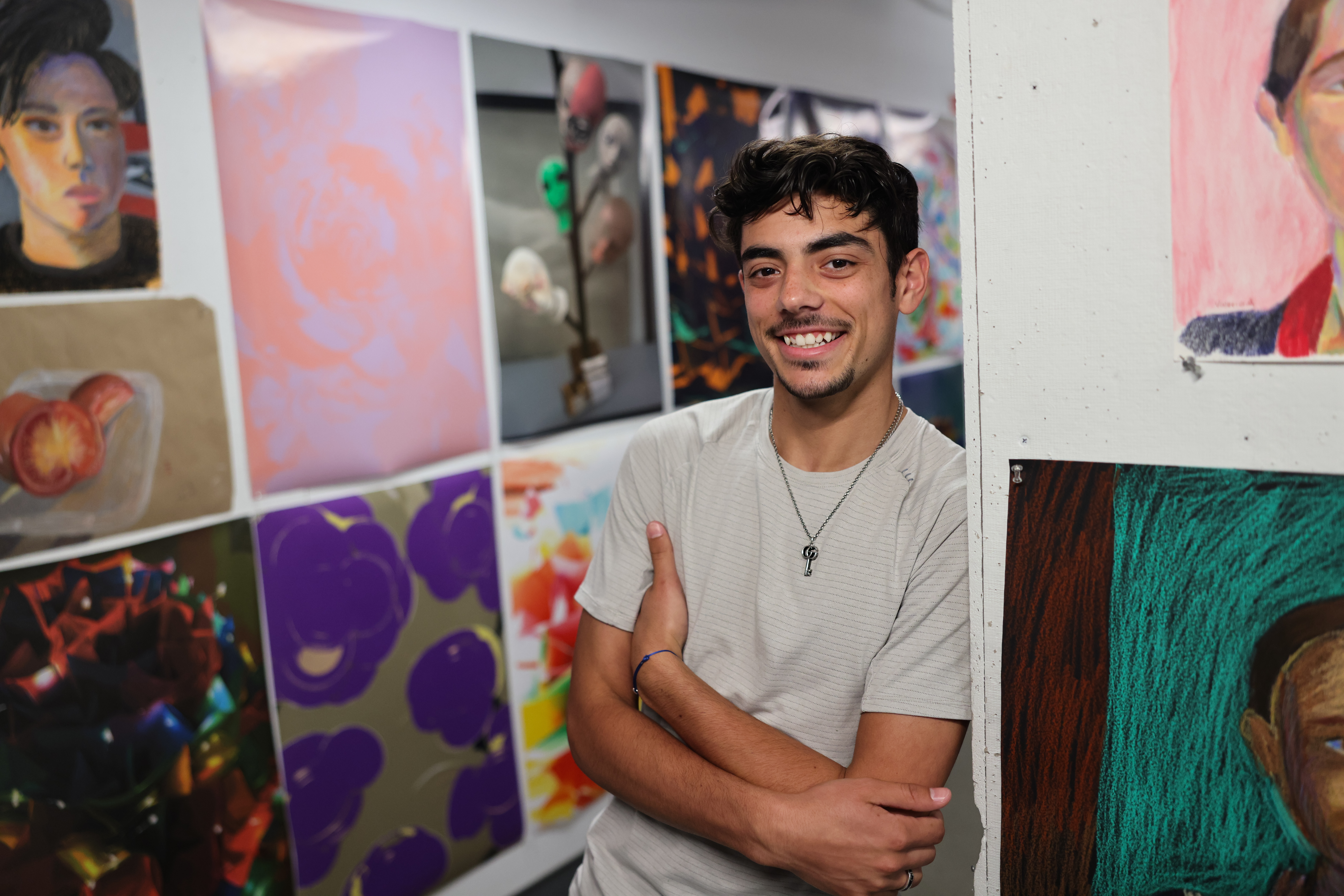 Latino male leaning against a wall with various types of artwork on it