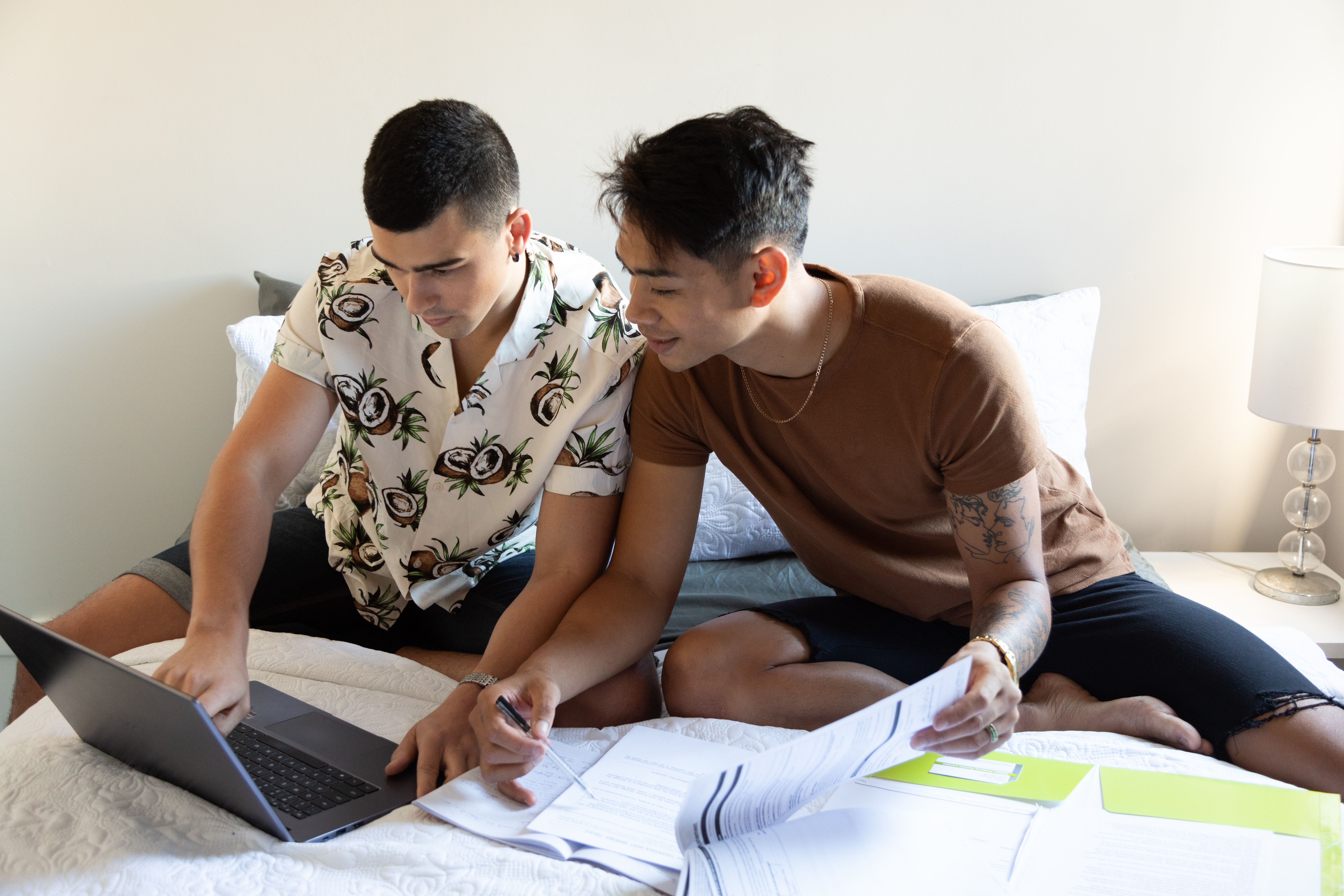 two men sitting on bed looking at paperwork