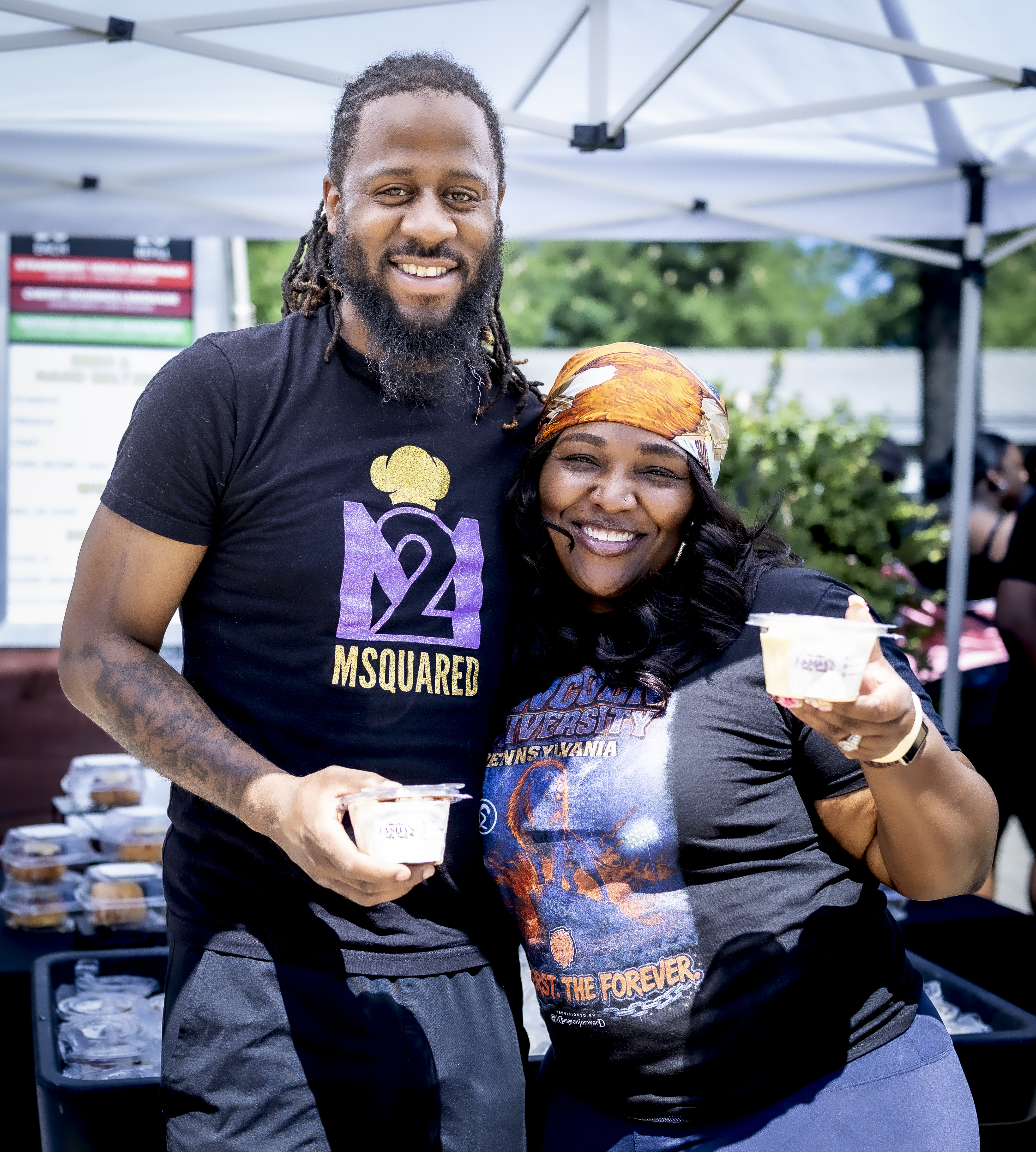 Tasha (an African American woman with black hair, wearing a black t-shirt and jeans), smiling and posing with an employee of MSquared