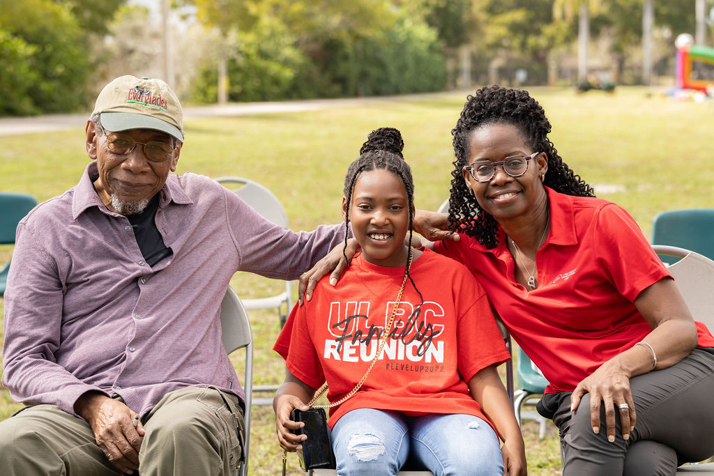 Young teenage girl in the middle of an older smiling man (left) and woman with dark, curly hair smiling (right)