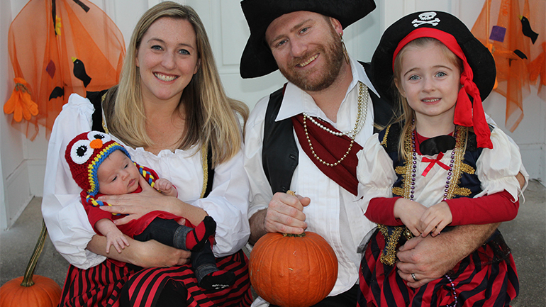 family picture of a man, woman, and two young girls dressed as pirates and parrot