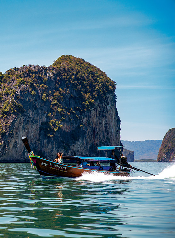 A traditional Thai boat in the sea in front of rocky islands. 