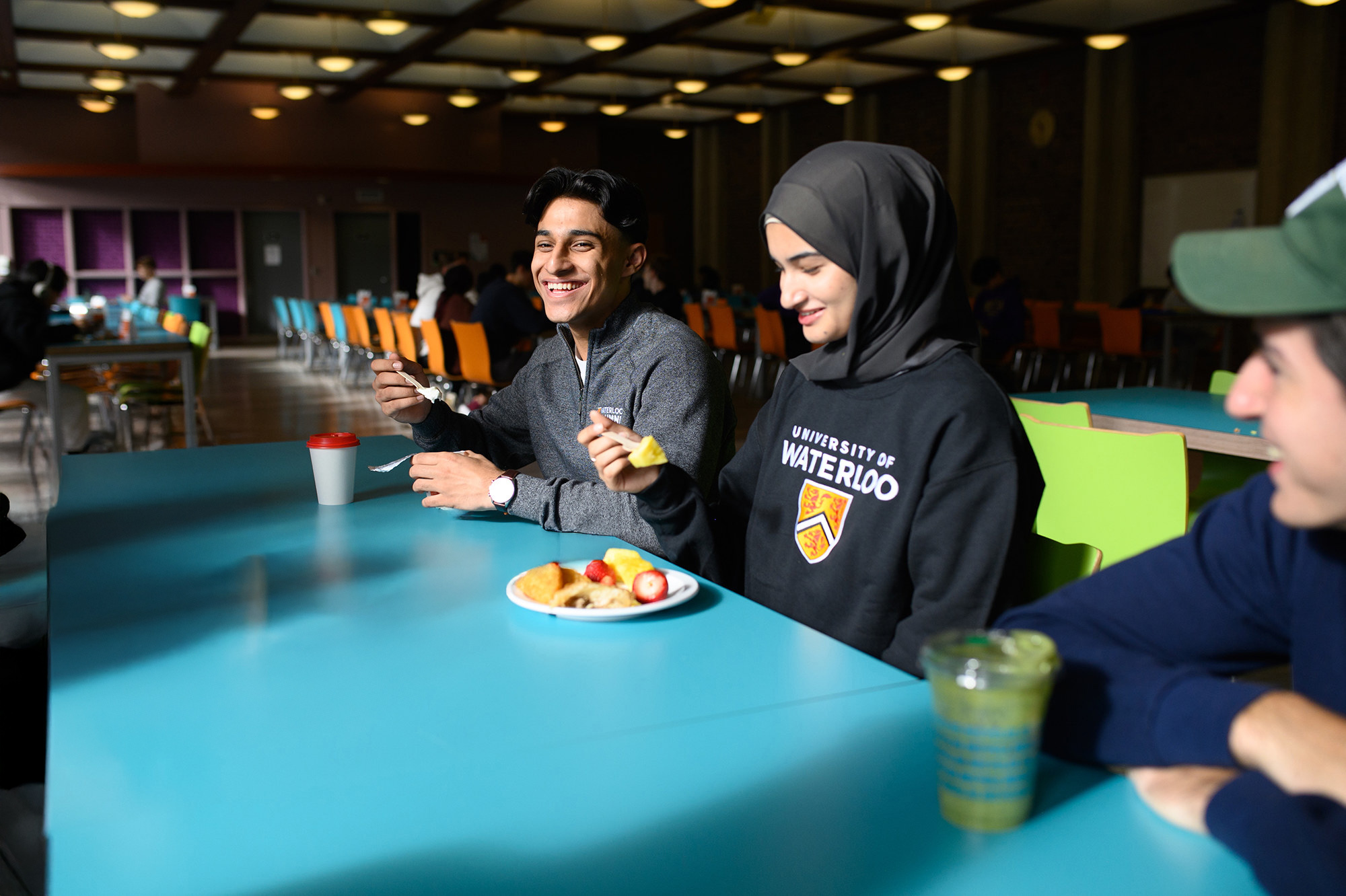 A group of students hanging out in the dining hall at their school residence, chatting and eating.