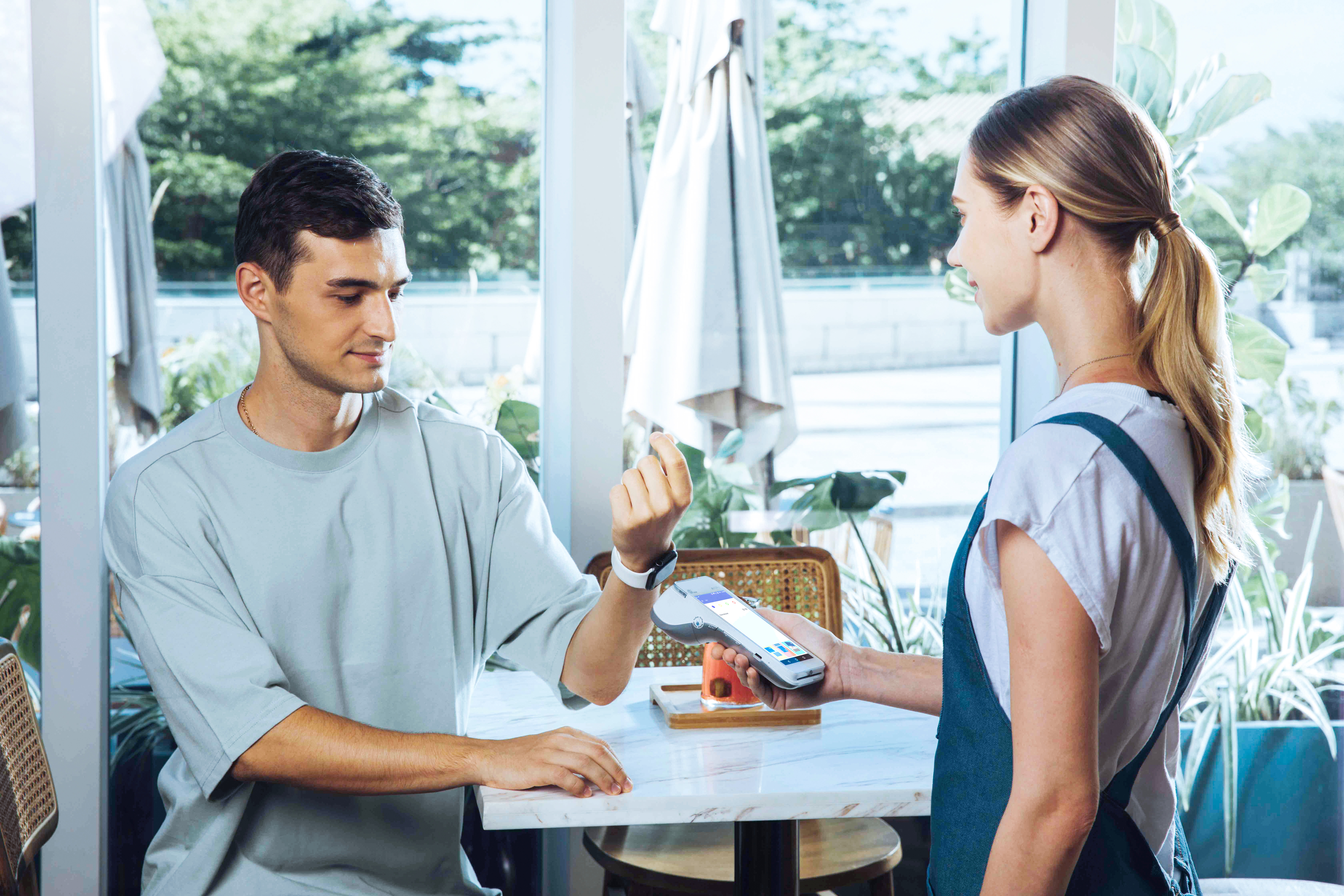 european male tapping to pay with smart watch onto physical terminal that is being held by the waitress