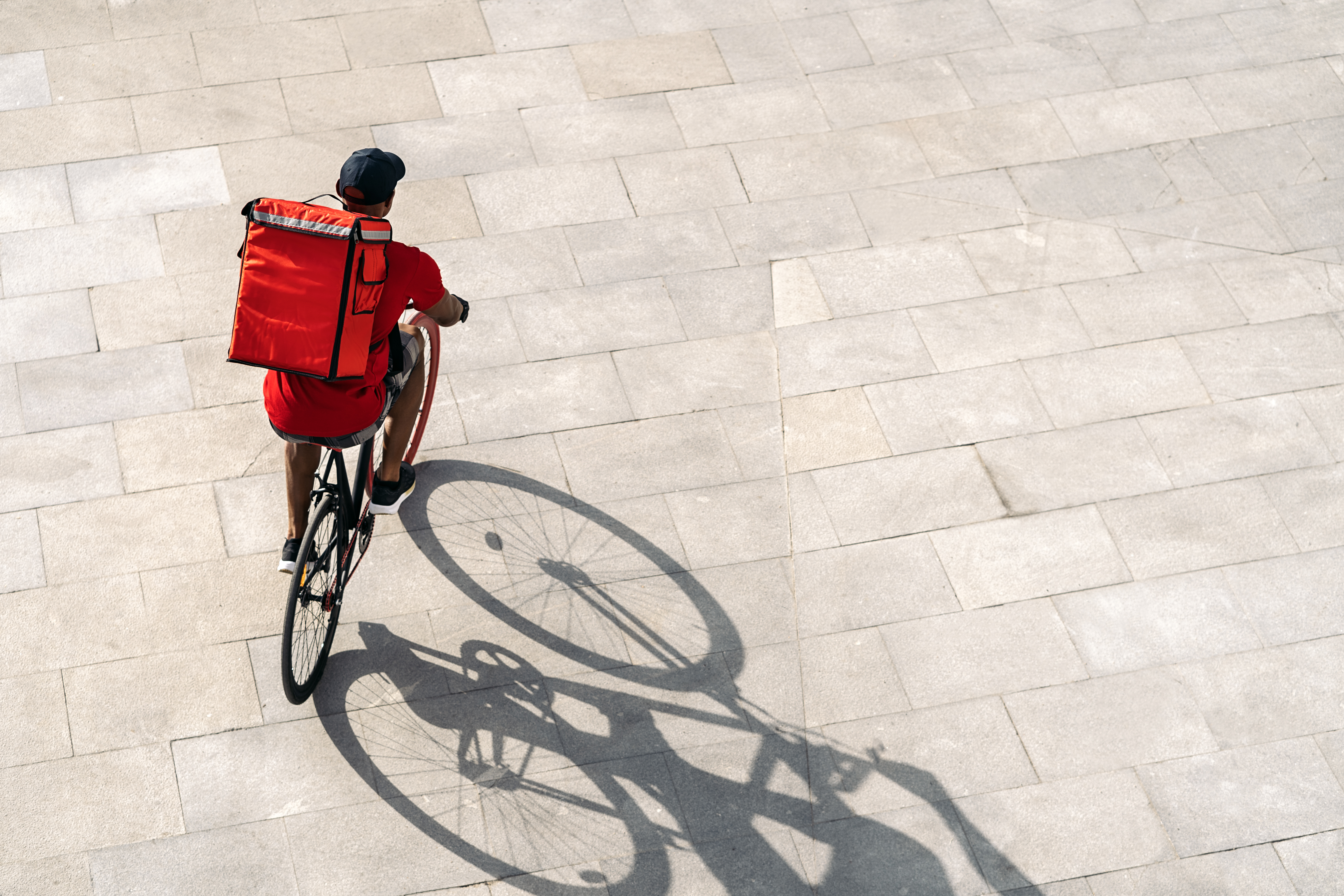 African delivery man wearing cap riding his bike in the city in his way to deliver a package.