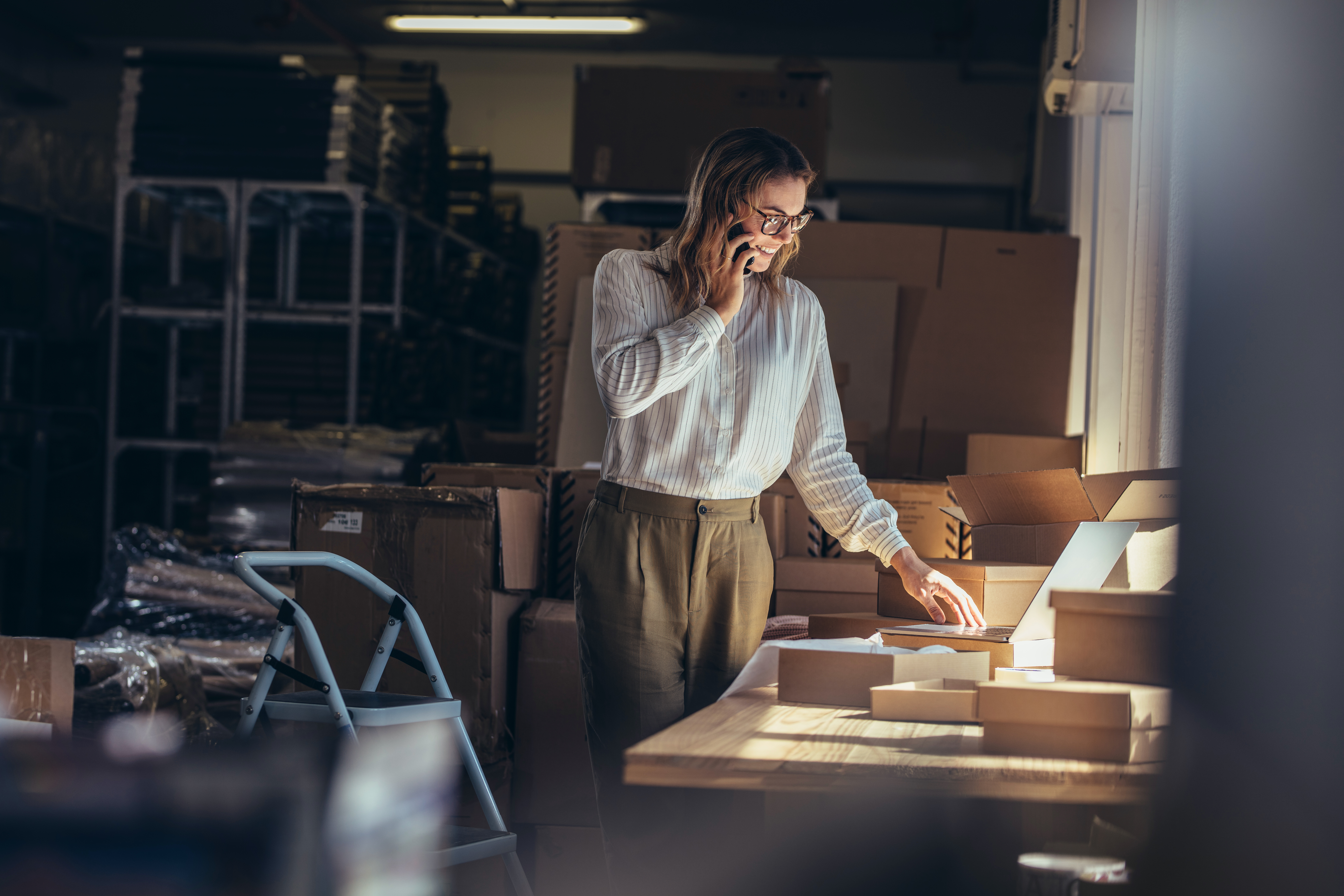 women in business casual on the phone in front of laptop and packages ready to ship