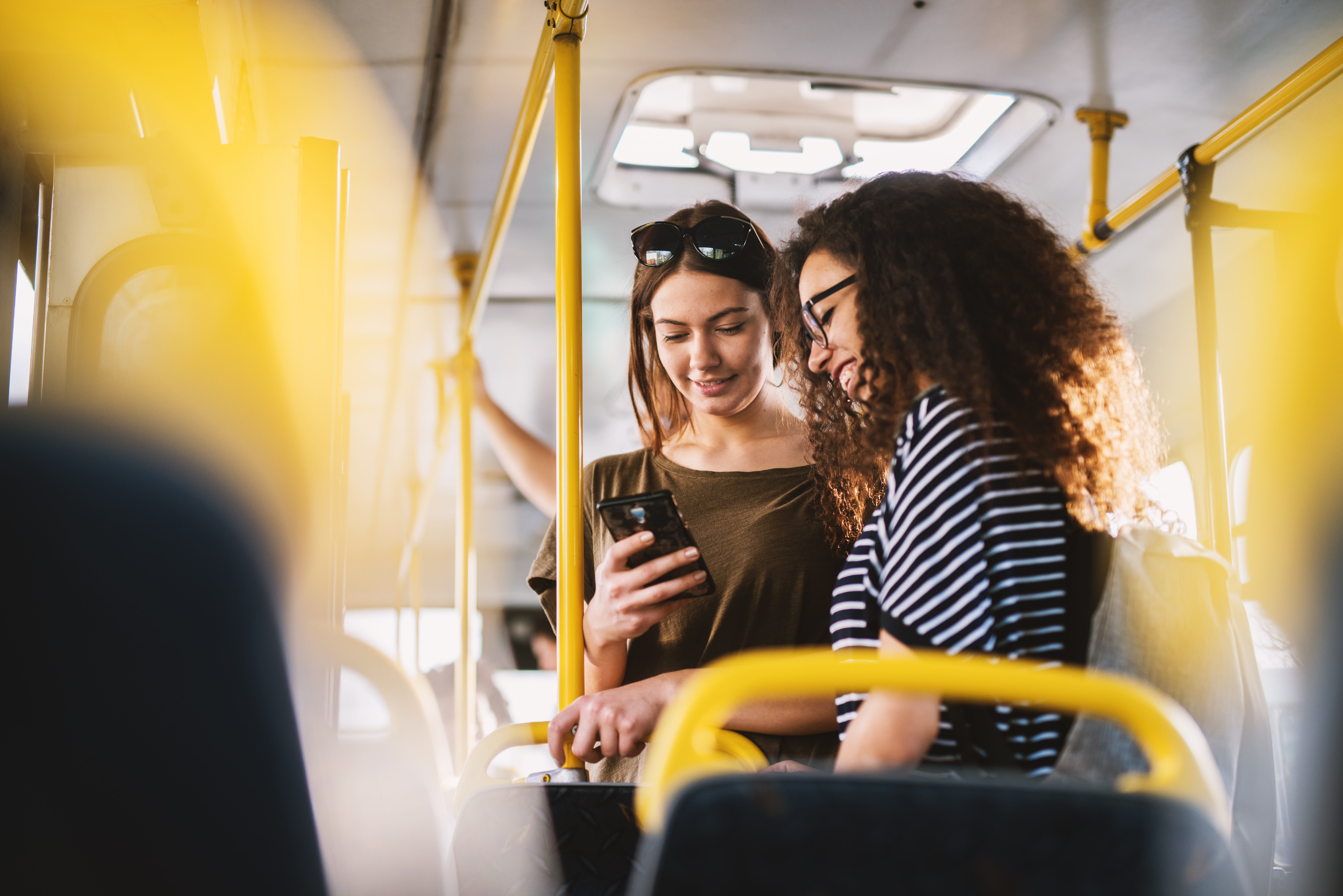 Two best young sweet girl friends standing in a bus and looking in a telephone.