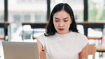 african american woman with short hair in button up collared shirt looking at credit card while having laptop in lap