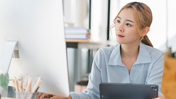 older man in blazer sitting at desk with laptop open in front of him on the phone