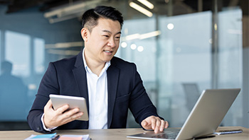 two business man next to each other on desk with one on laptop and other writing