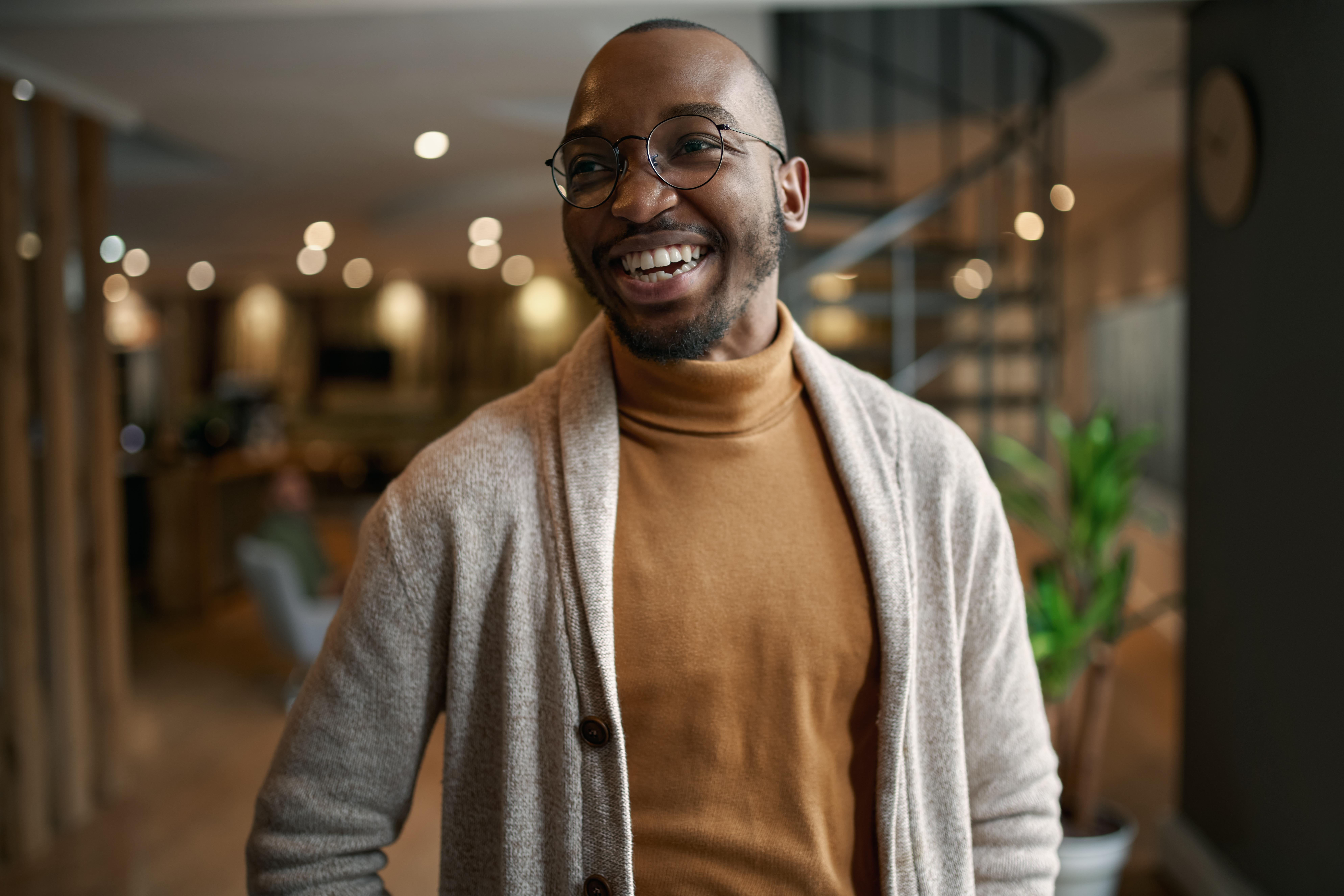 Happy portrait of african entrepreneur laughing and smiling. feeling excited and positive. Wearing trendy clothing and eye glasses in a modern working space