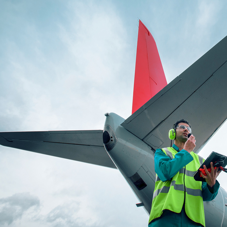 Aeronautical engineer in front of an airplane wearing ear protection talking into a handheld device.