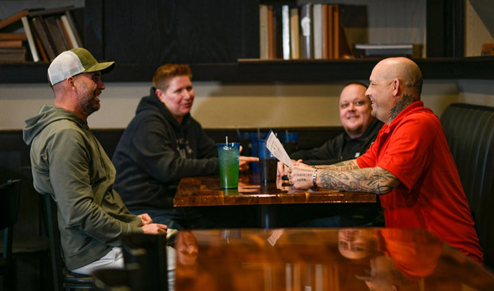 Wounded warriors Philip Krabbe, Ben Merrill, Lisa Juve, and Chris Maki are sitting at a restaurant talking. 