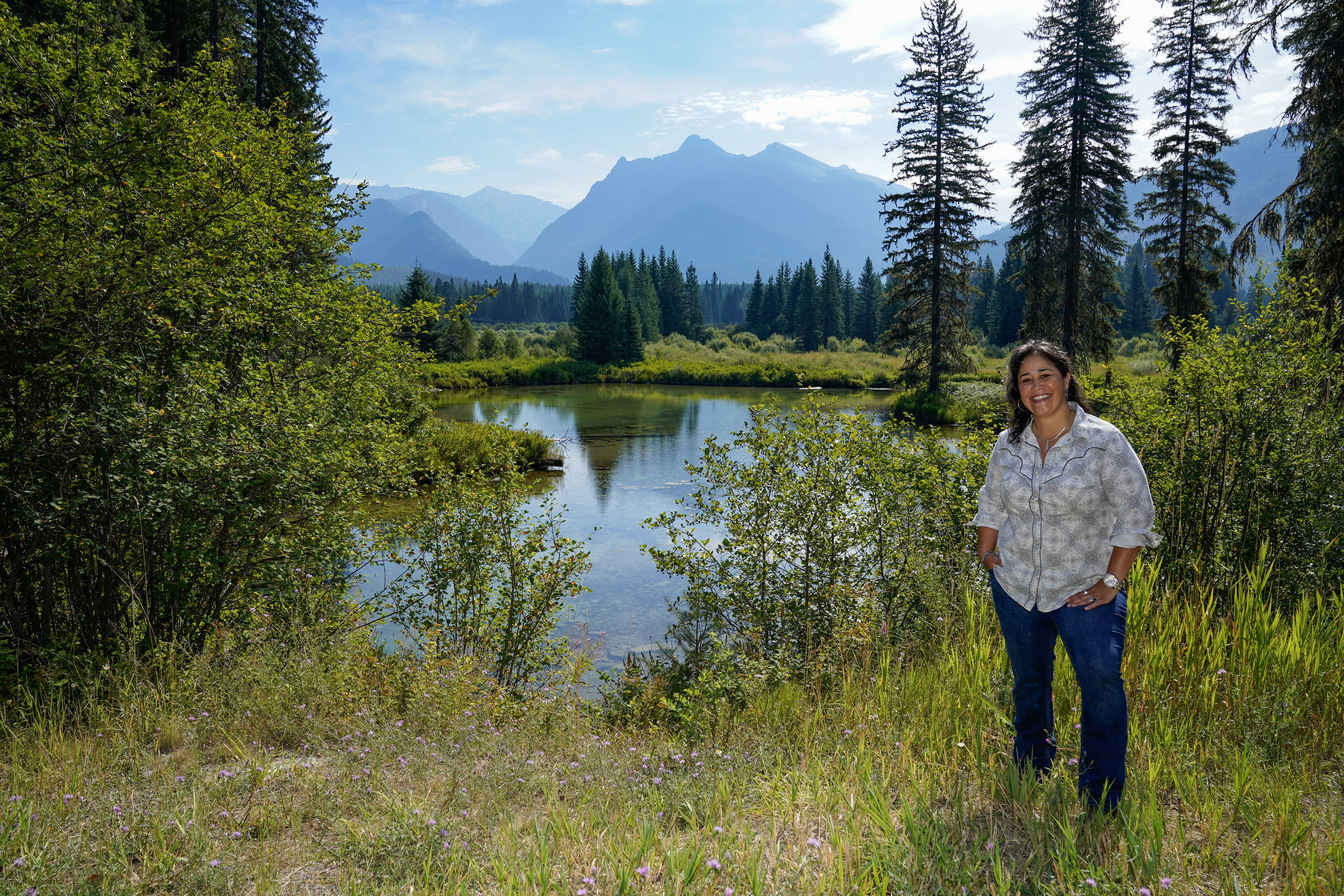 WWP warrior Tina Waggener stands in front of a pond with her hands in her pockets and smiling.