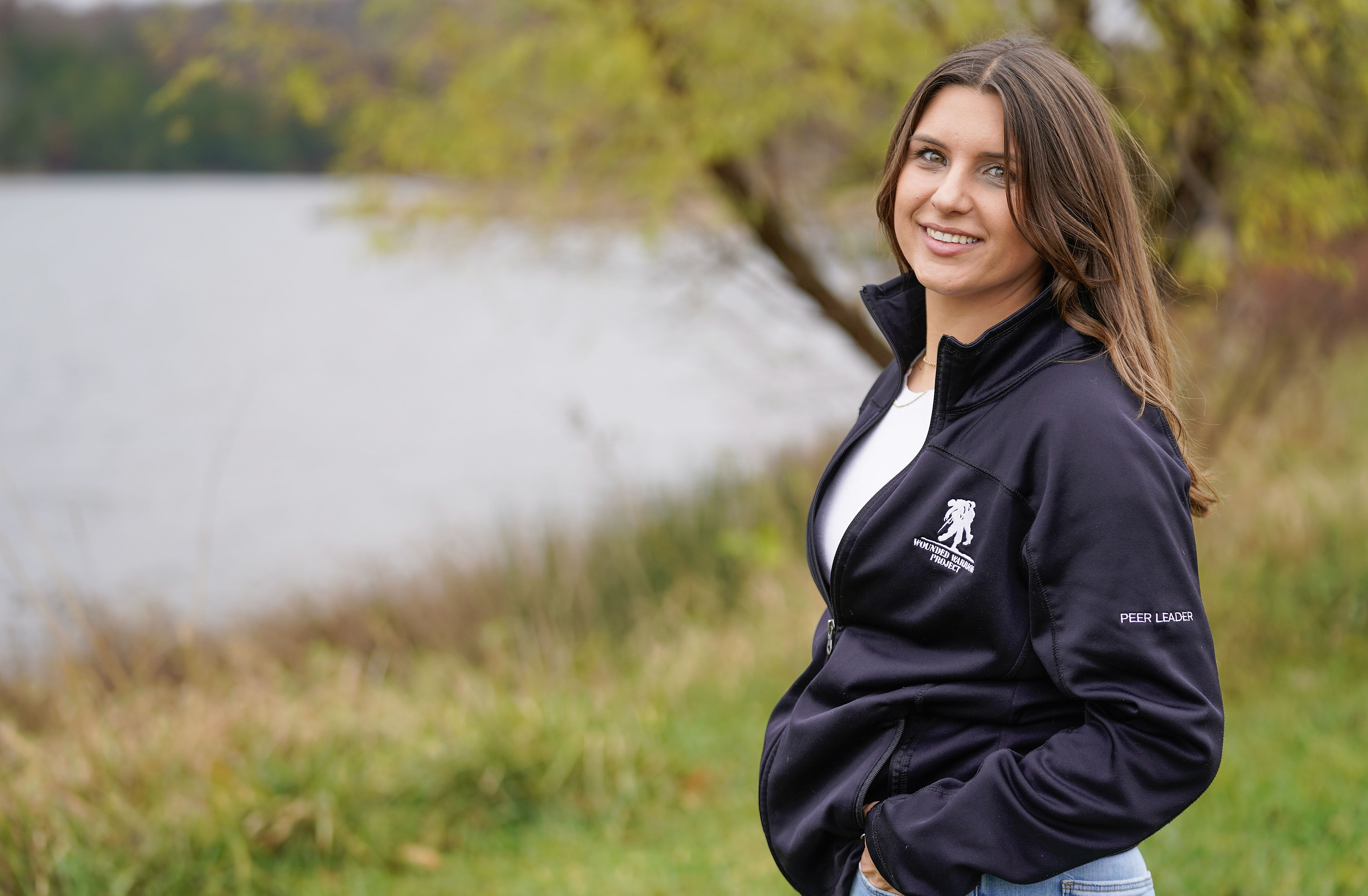 Wounded warrior and peer leader Keara Torkelson stands outdoors in a black WWP jacket, smiling warmly at the camera.