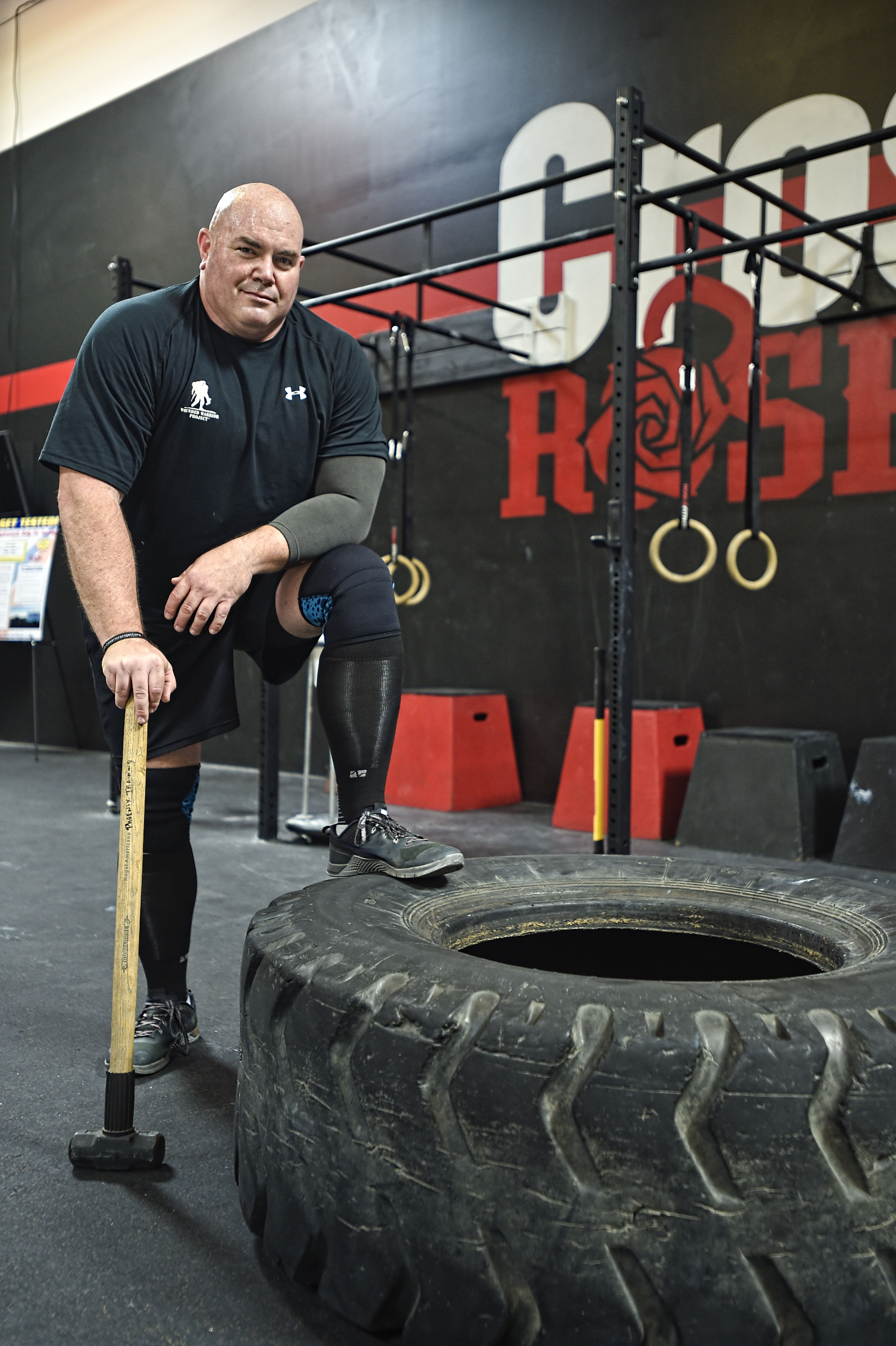 During a CrossFit workout session, wounded warrior Bill Hansen stands with one foot over a large tire holding a sledgehammer.