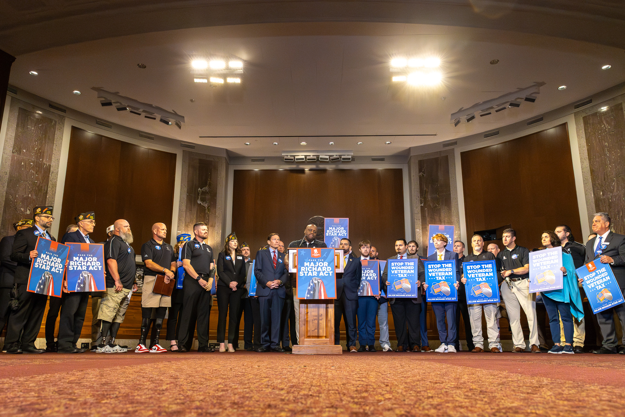 Five wounded warriors sit in an office around a table smiling with papers in front of them that cover the bills they would like to see passed during this Congress. 