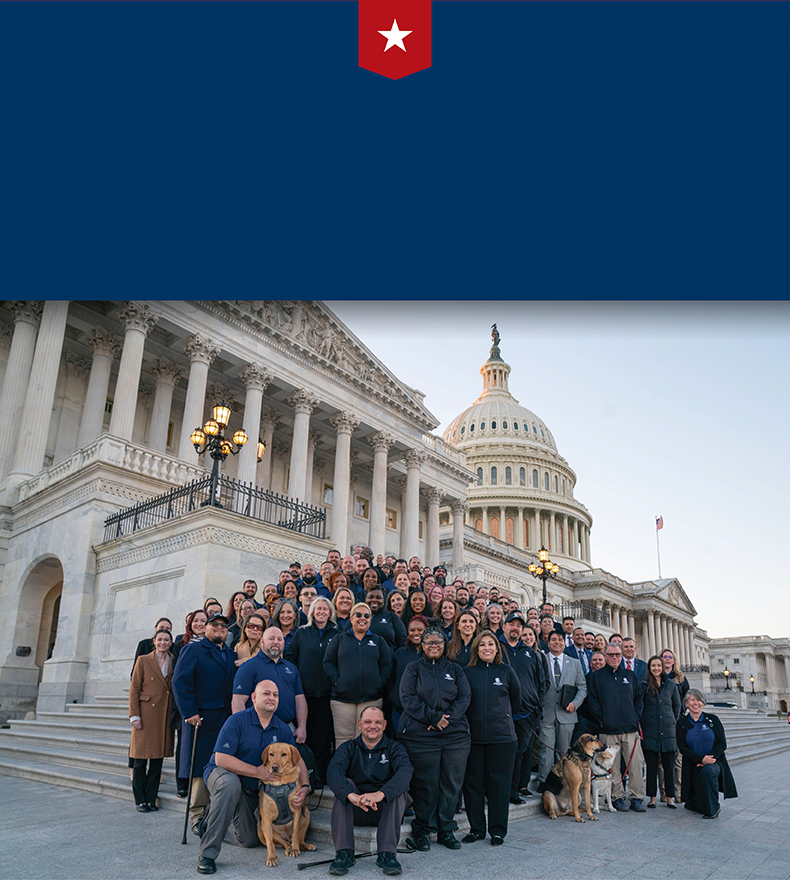 Wounded warriors in blue tops stand/sit on the U.S. Capitol steps in D.C. Several service dogs are visible nearby.